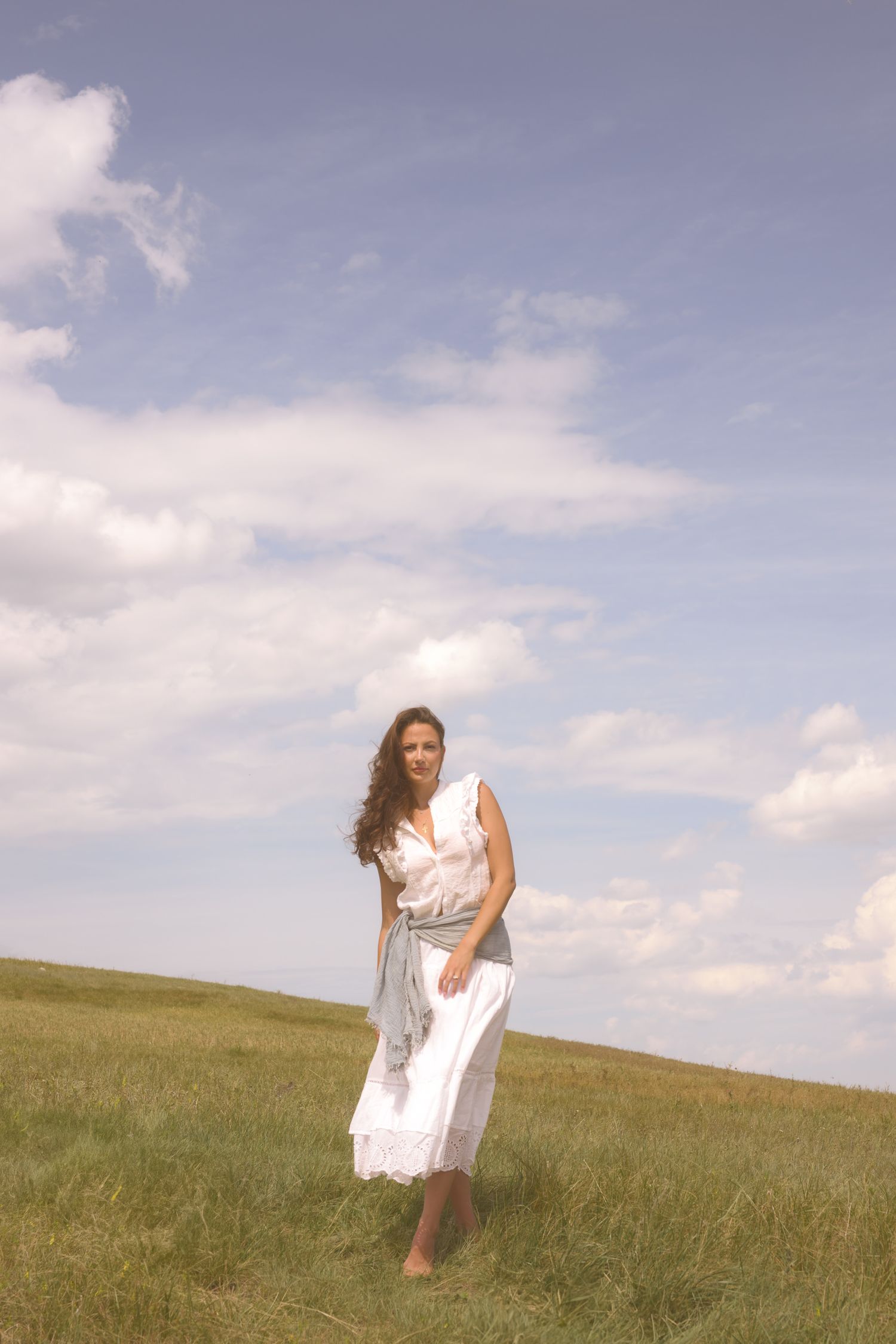 A dreamy summer scene with a figure in white standing on a rolling hillside.