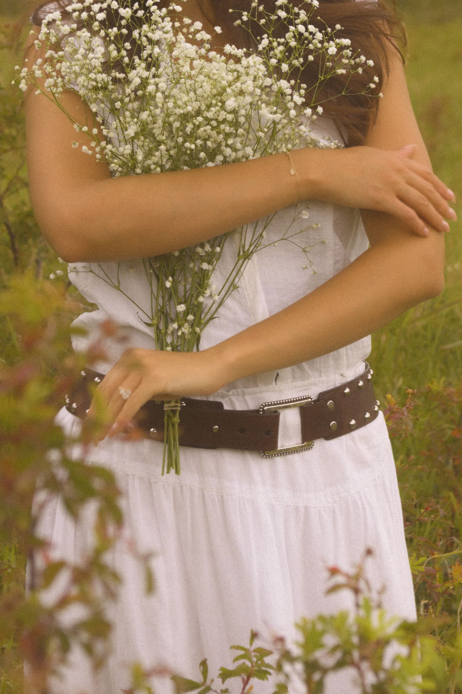 Delicate baby's breath flowers are held against a white dress with a studded brown belt.