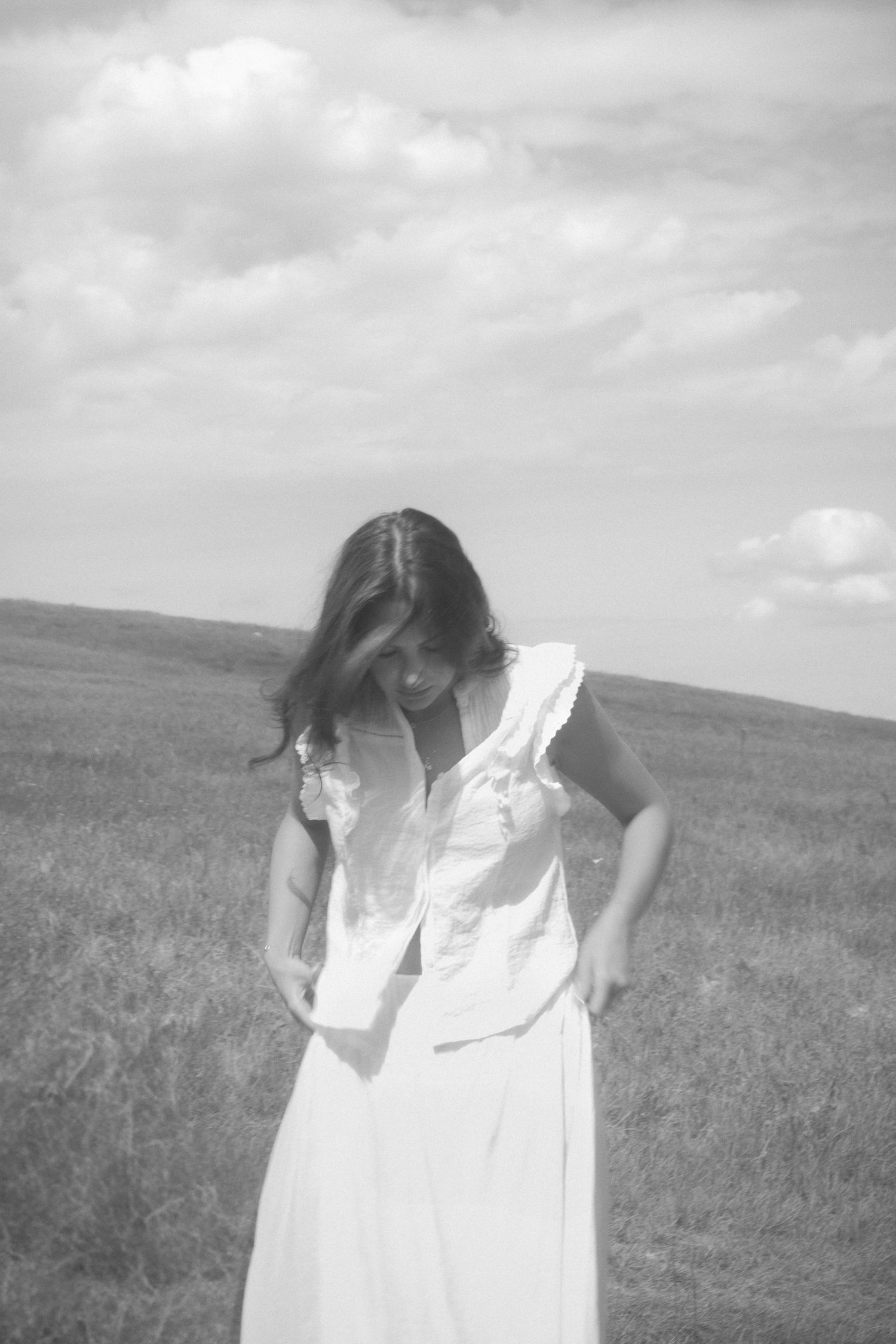 A black and white portrait of someone in a white dress looking down thoughtfully.