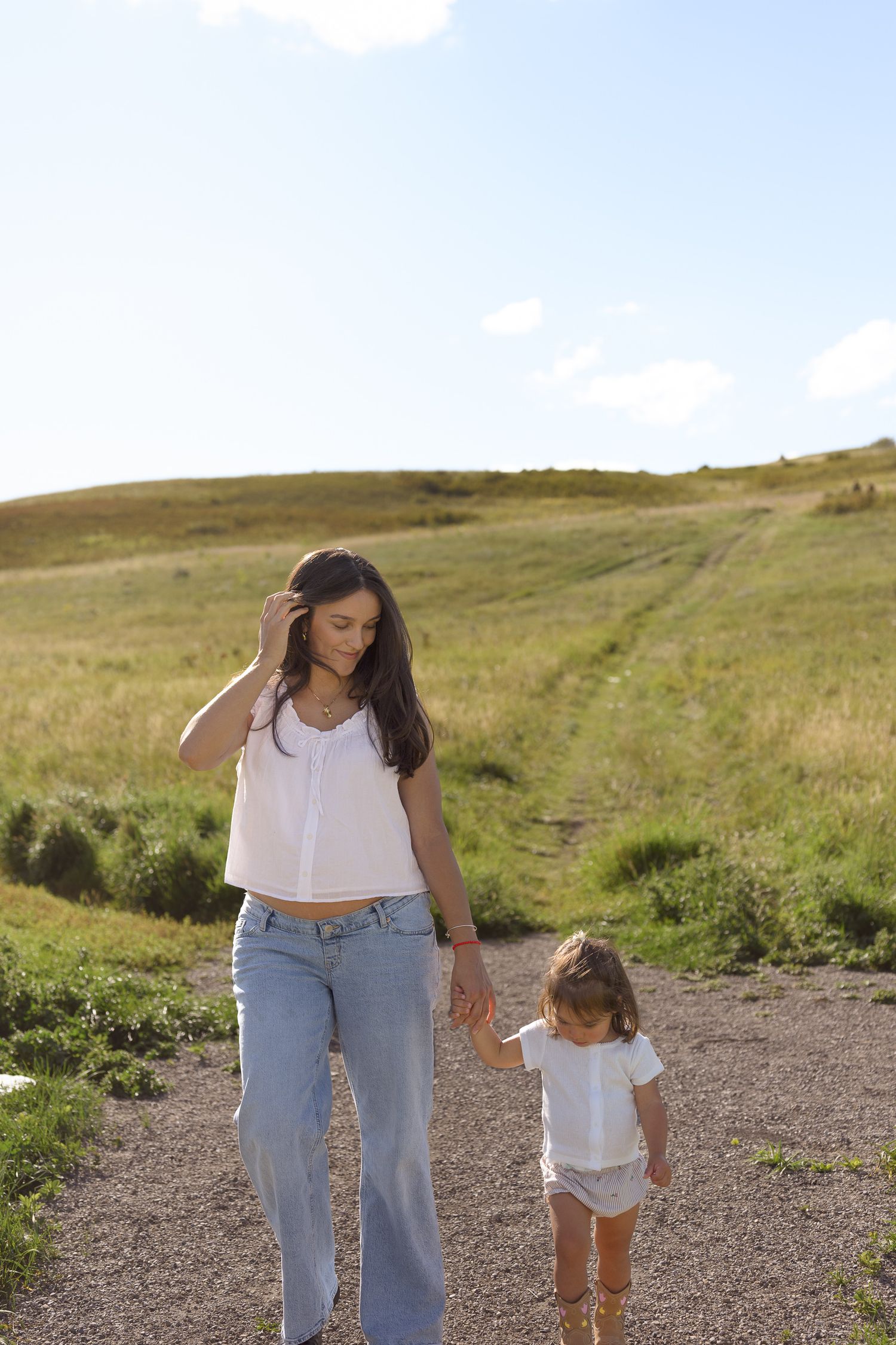 Mother and child walking together on a scenic hillside path.