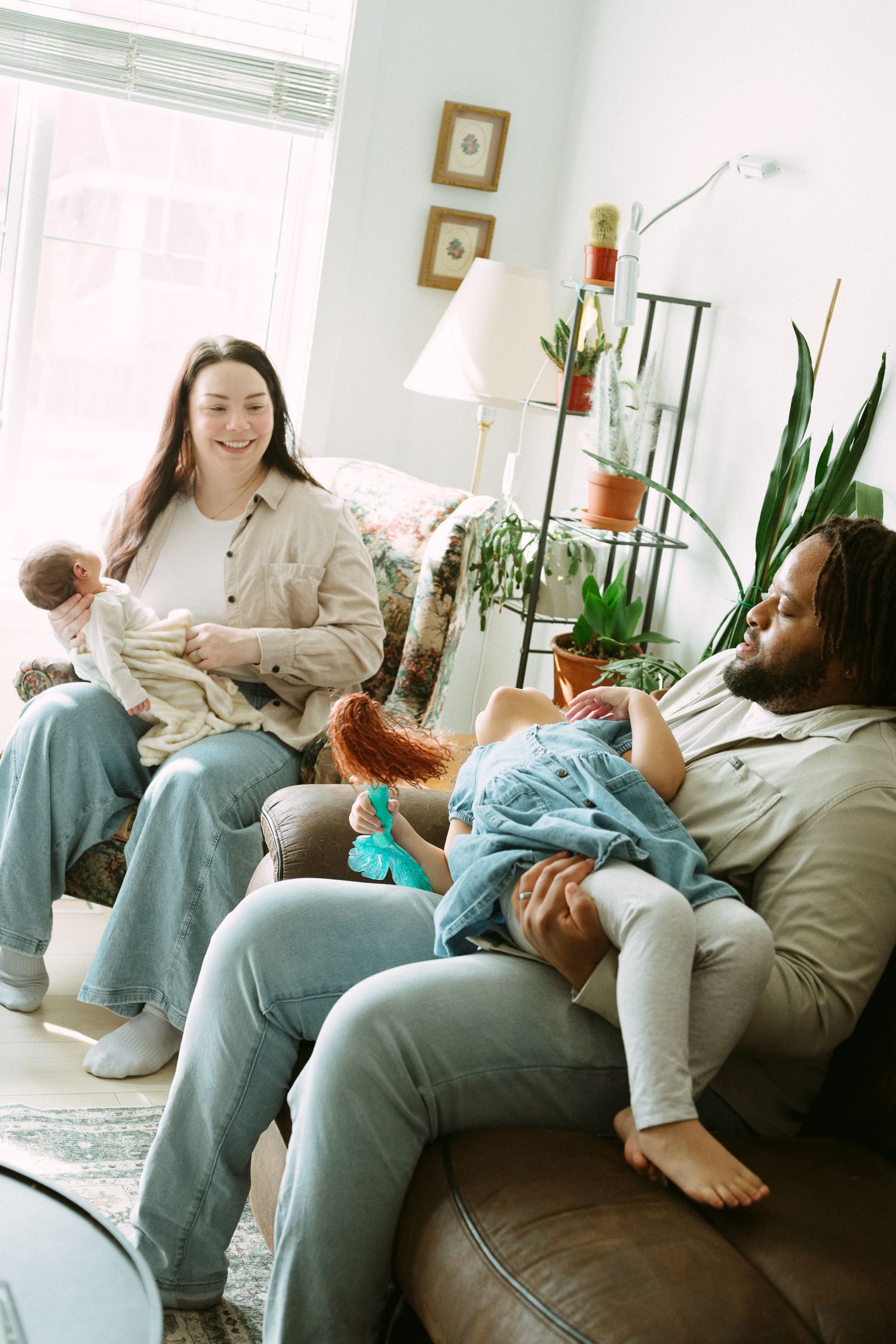 A happy family relaxing on a leather sofa, with a woman holding a baby and a man playing with a child.