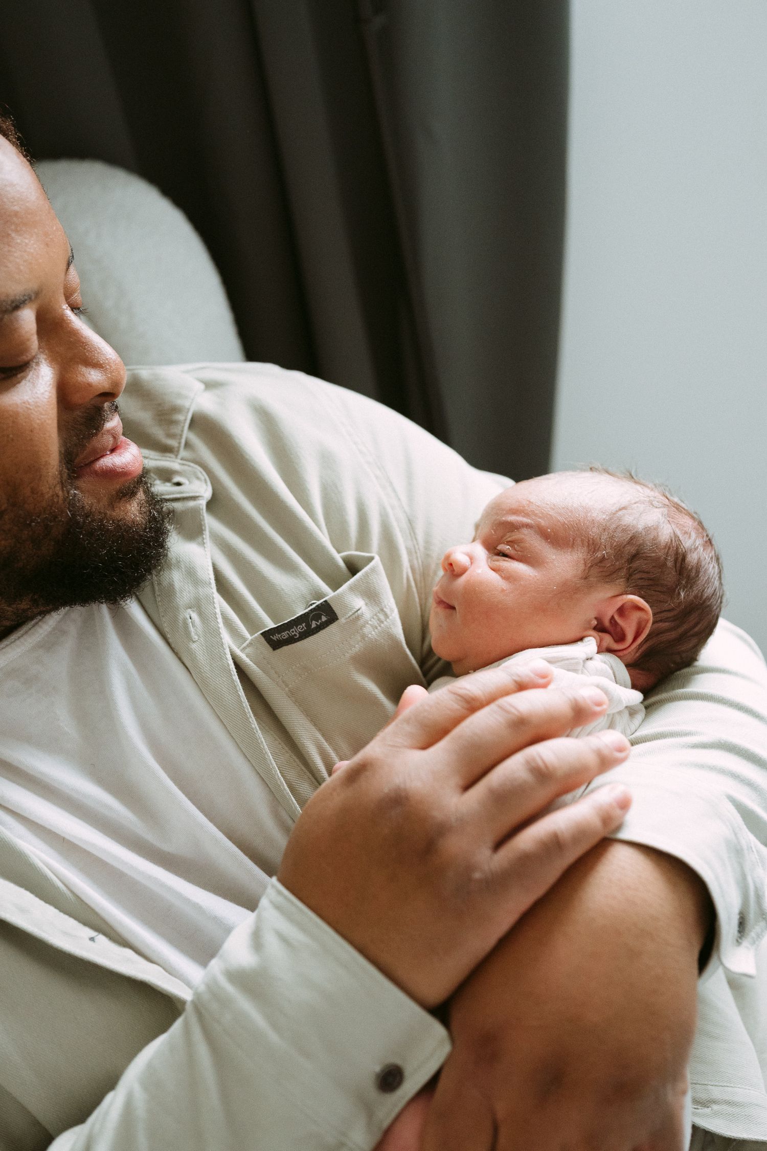 A bearded father tenderly cradles his newborn baby in his arms, gazing lovingly at the infant.