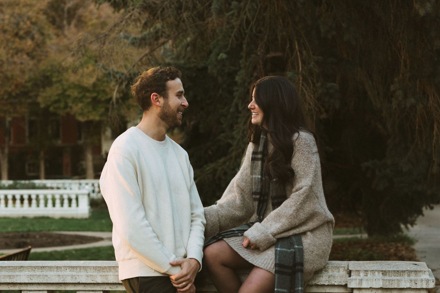 A couple sits together on a wooden bench in a park during sunset.