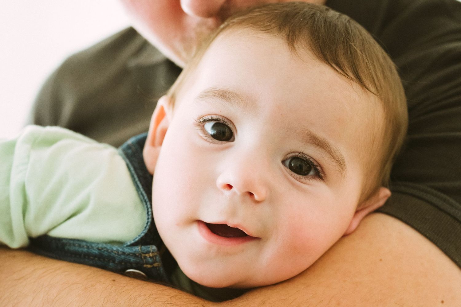 Close up view of a small child resting on someone's shoulder with a bright expression.