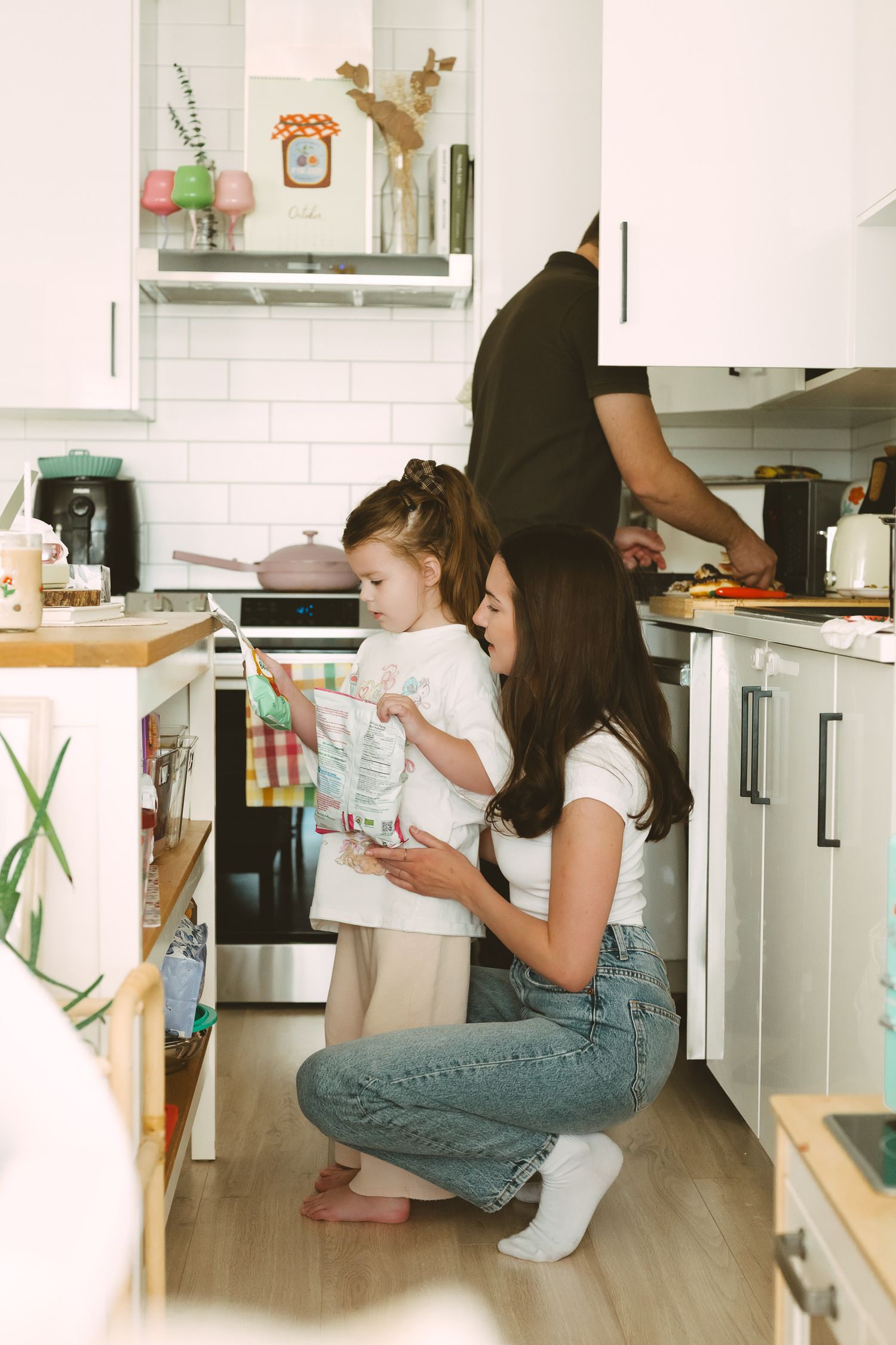 Woman in white t-shirt and jeans cleaning kitchen cabinets and organizing items at home.