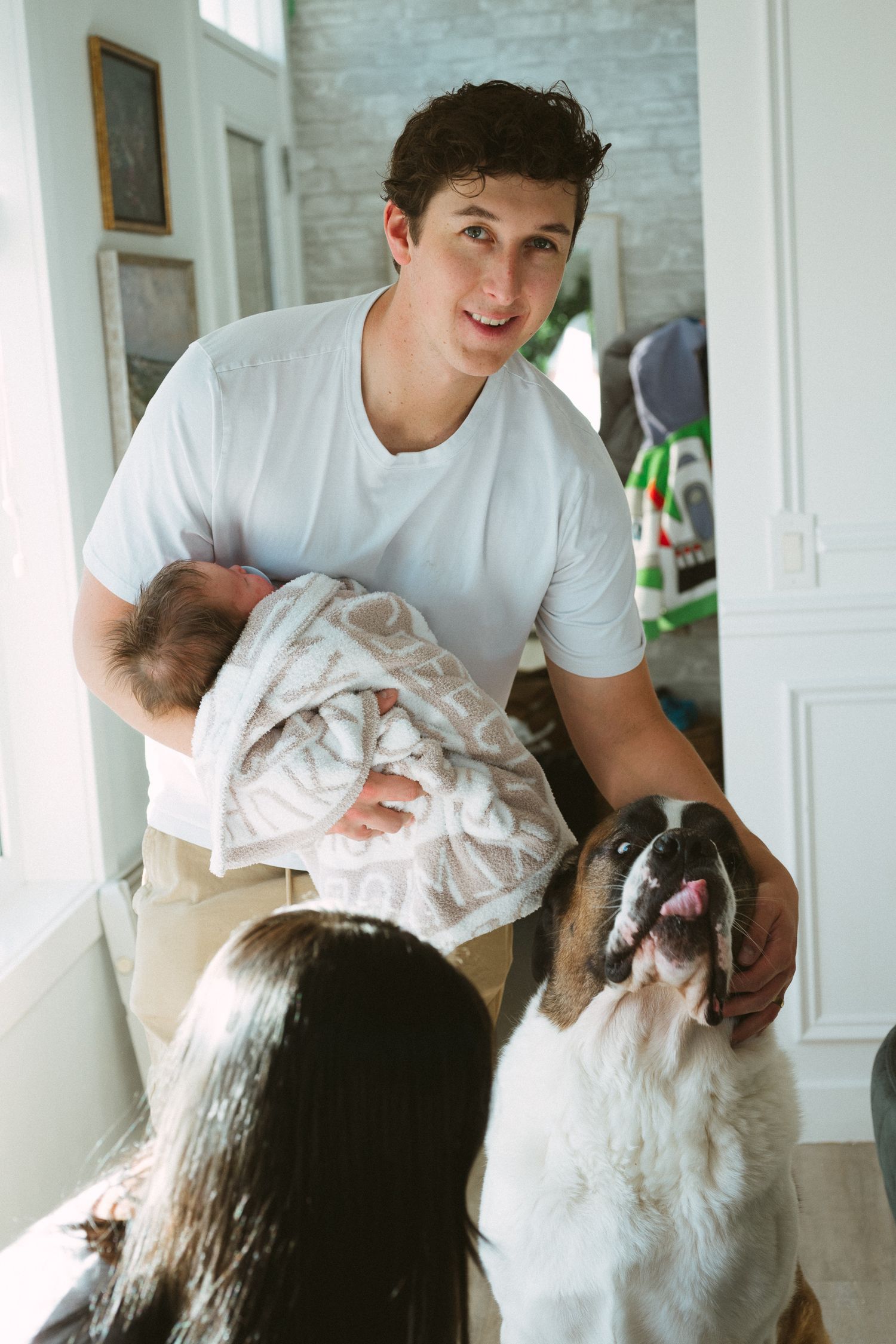 A family moment at home with a large Saint Bernard dog and a baby wrapped in a white blanket.