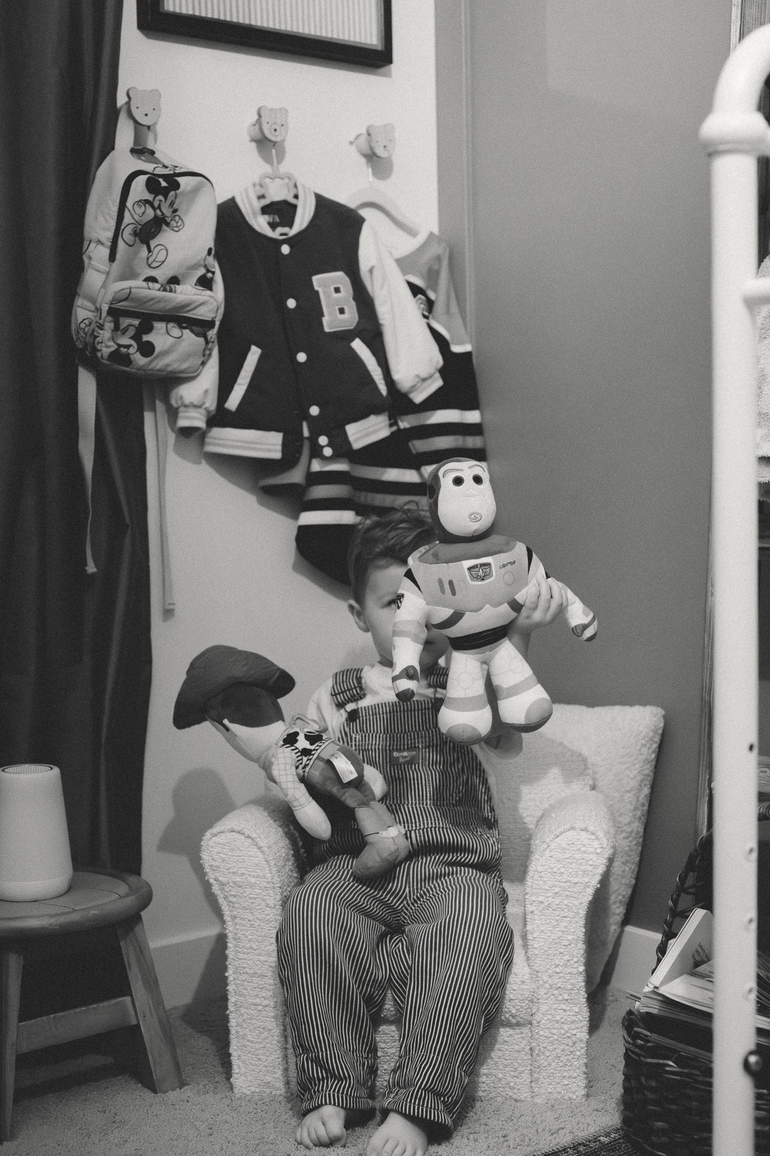 A black and white photo showing someone sitting in an armchair with stuffed toys including Buzz Lightyear and Mickey Mouse.