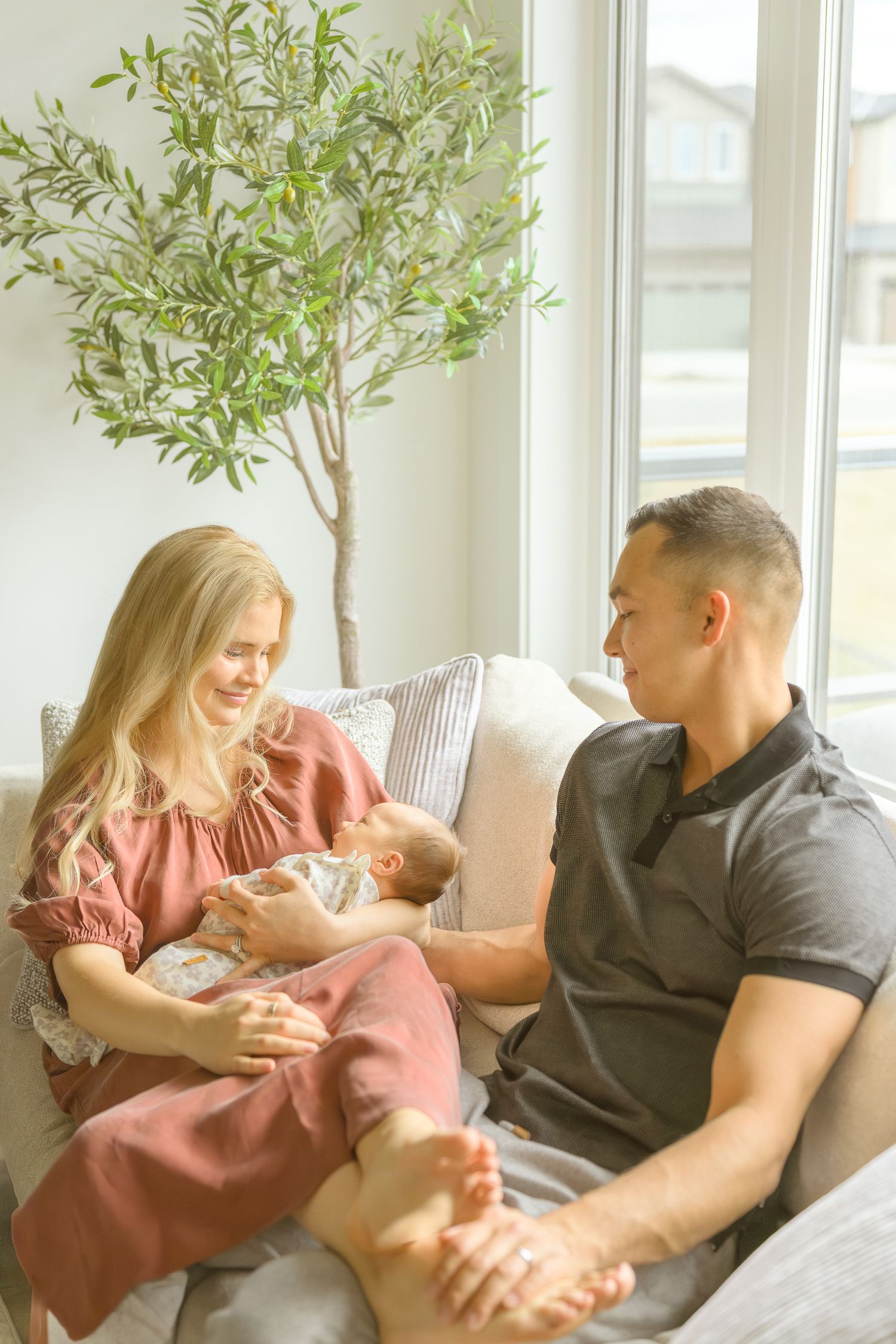 Couple shares tender moment with newborn on couch beside indoor plant.