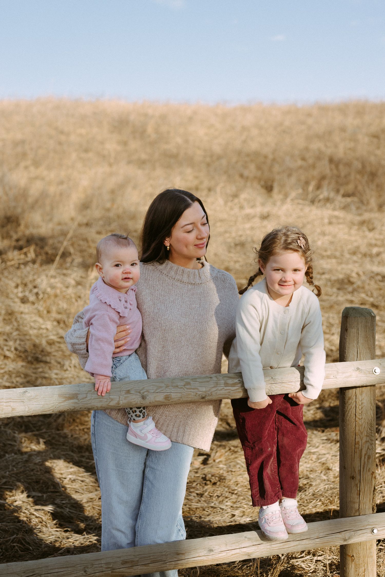 Children sitting with adults on a wooden fence in a golden field during sunset.