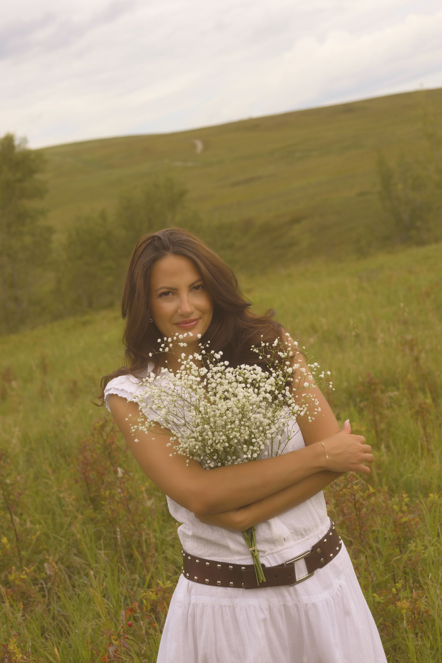 Someone embraces a bouquet of baby's breath while standing in a green summer field.