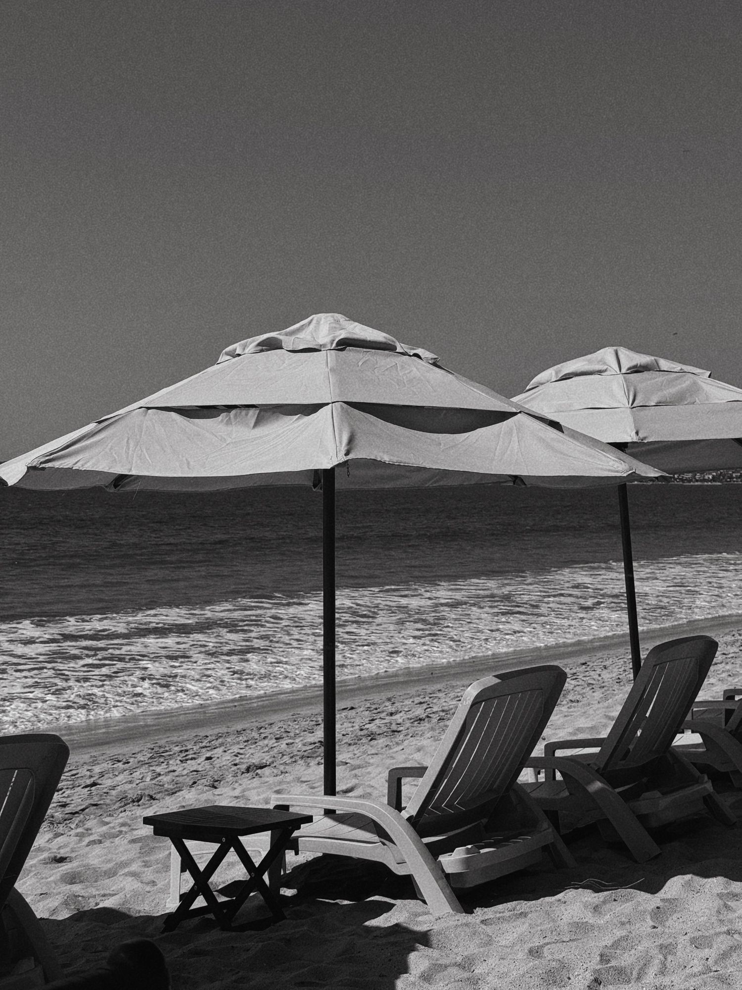 Beach scene with white umbrellas and lounge chairs along the shoreline in black and white.