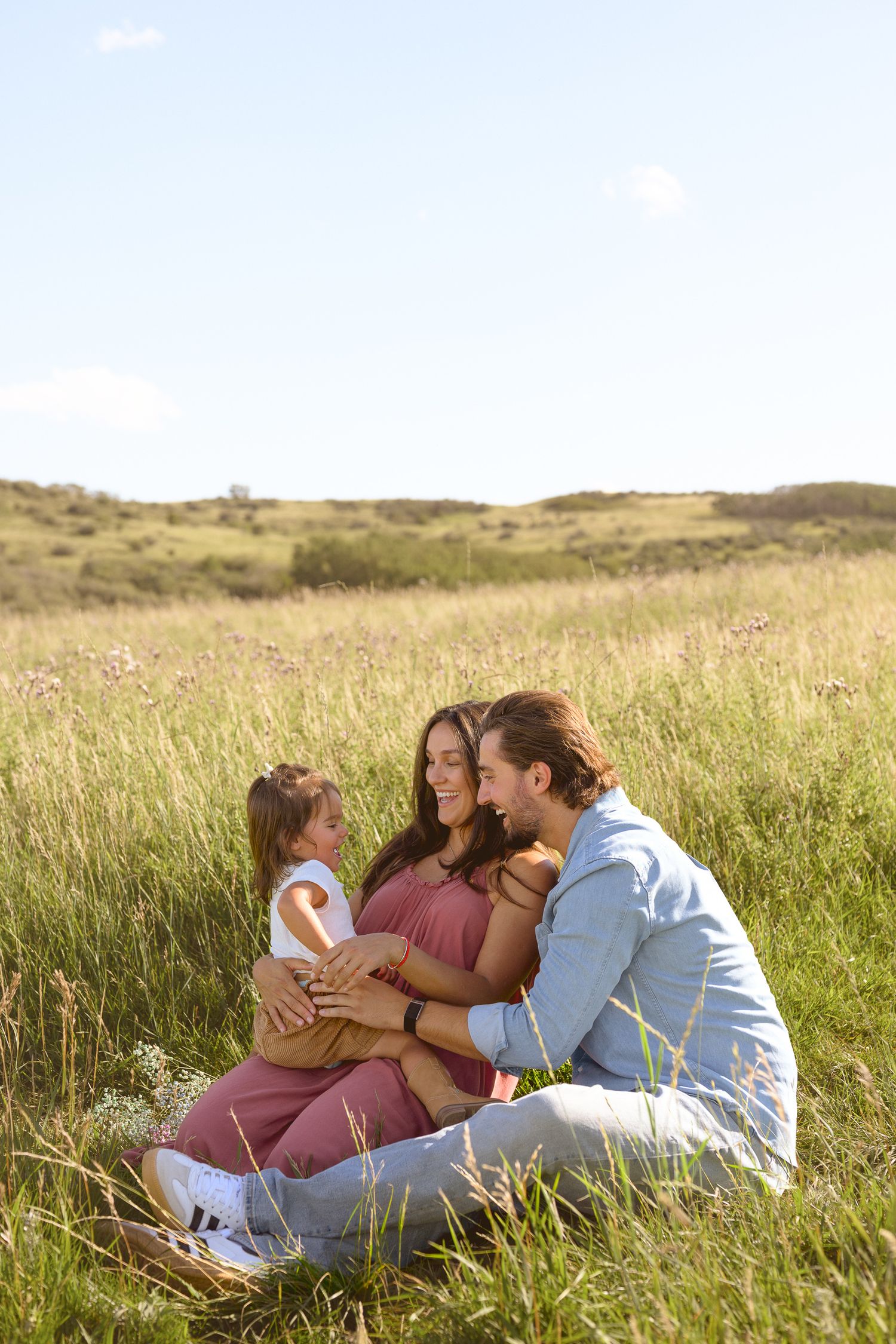 Family sitting together in tall grass field during golden hour.