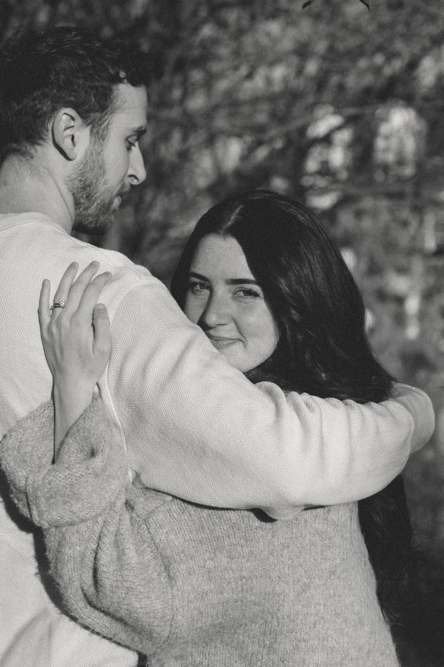 A romantic black and white photo series showing a couple embracing in an outdoor setting with trees in the background.