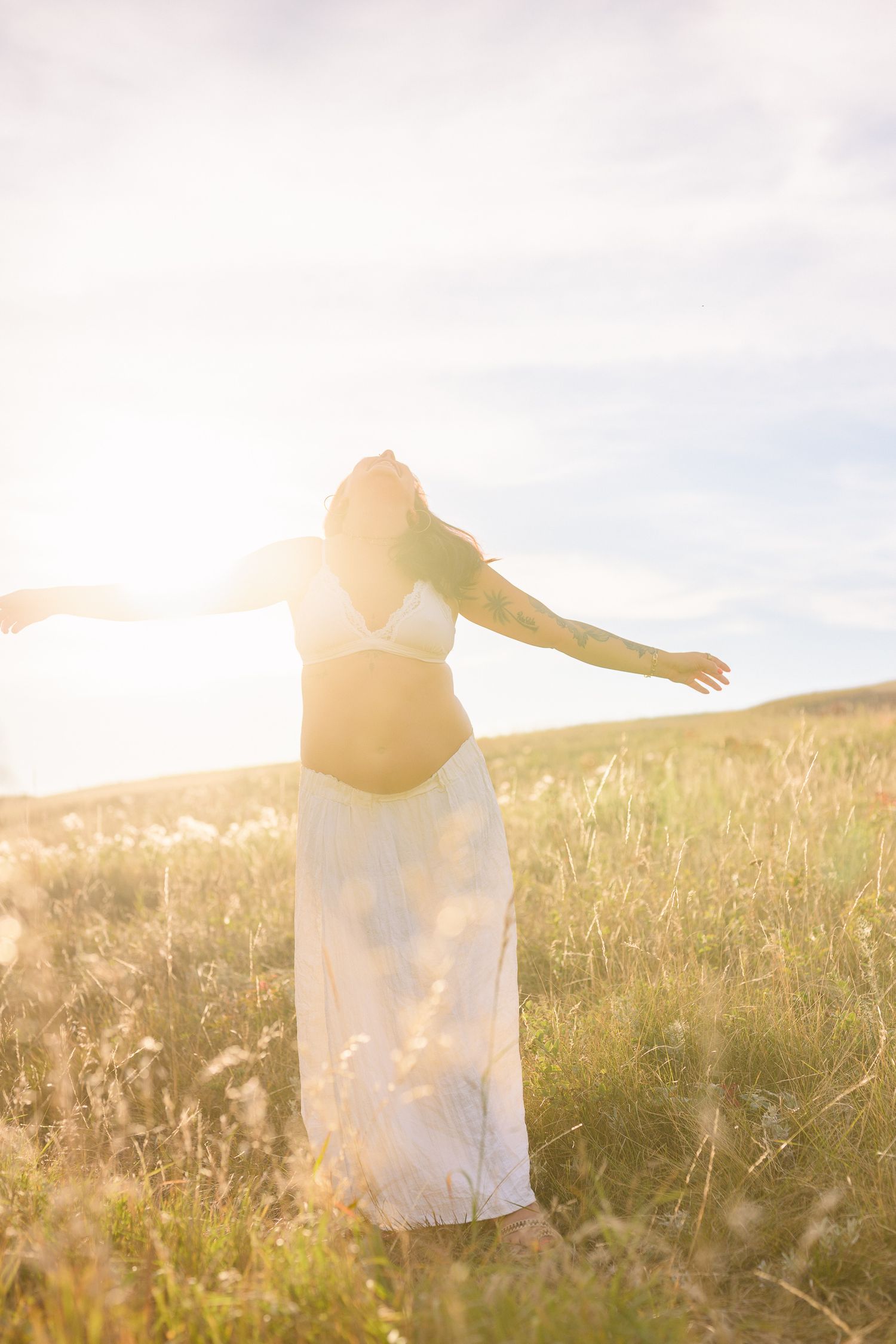 Silhouette of person with arms outstretched in sunlit meadow.