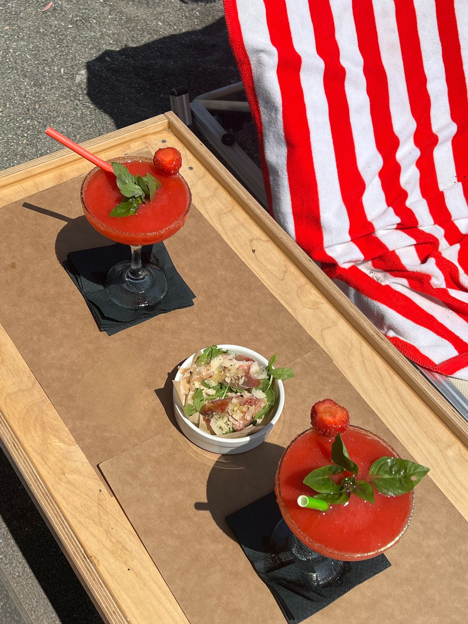 Red cocktails and appetizer served on wooden tray with red and white striped towel.