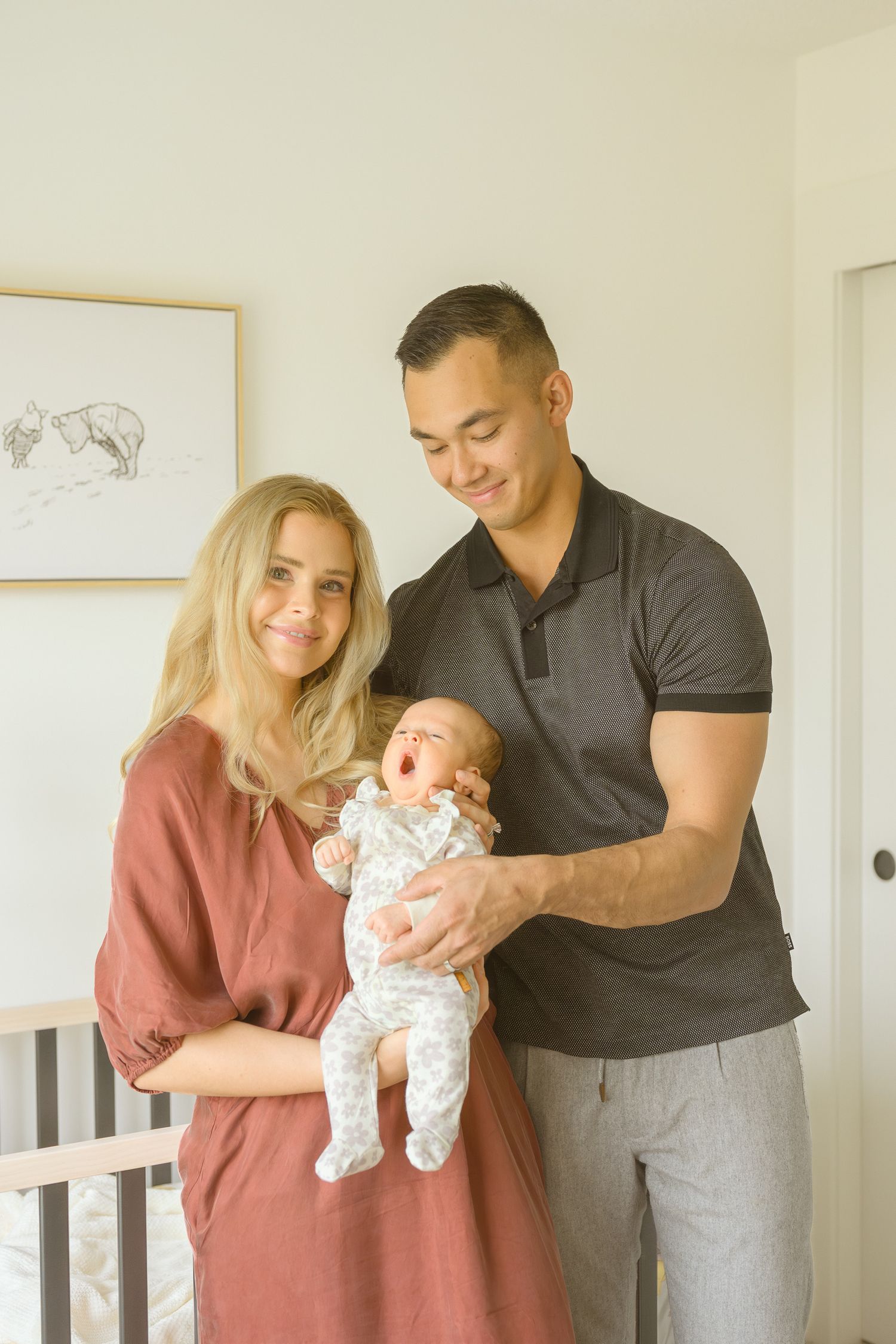 A couple smiles while holding their baby in a nursery with minimalist wall art.