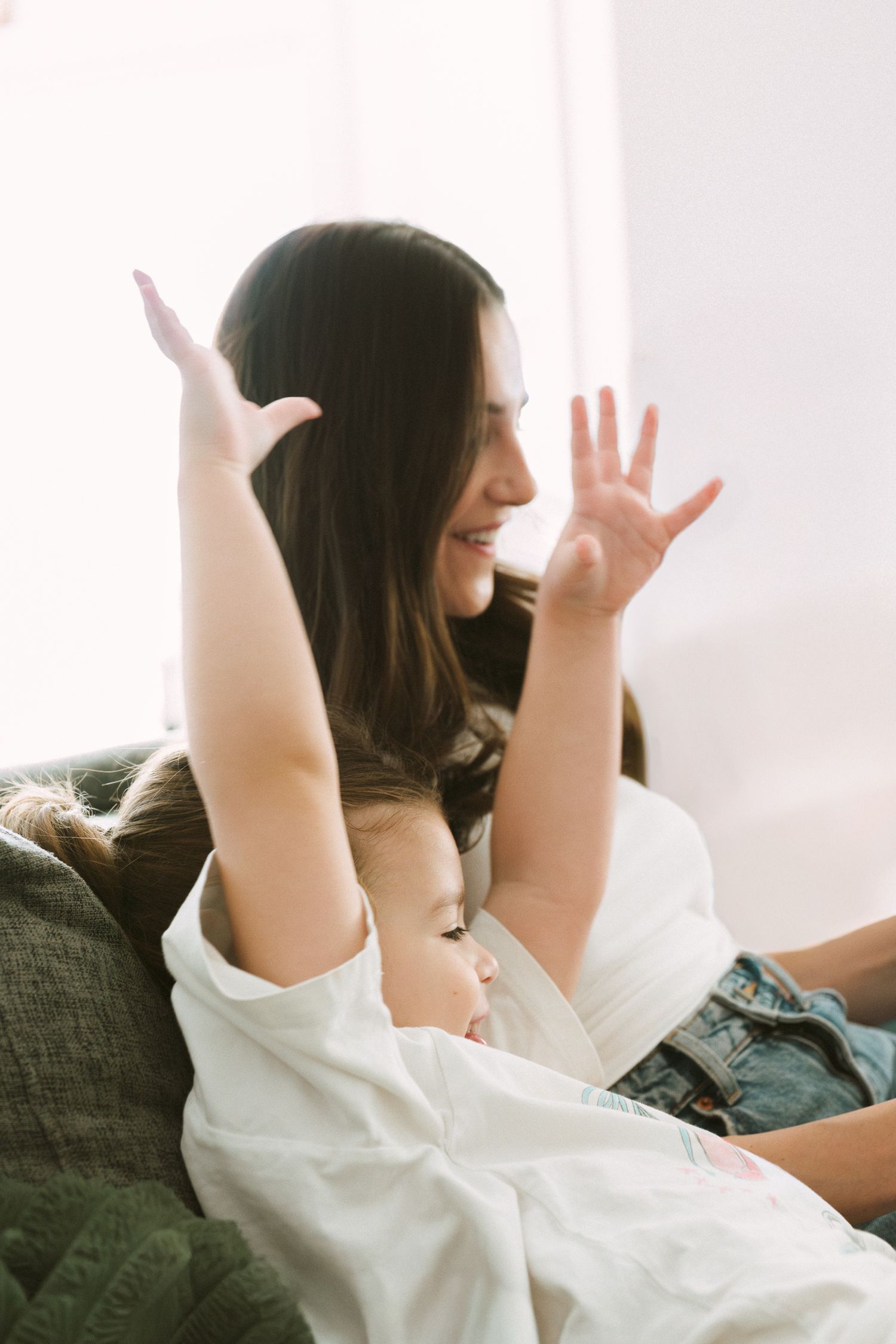 A person in white lounges playfully on a couch with raised arms.