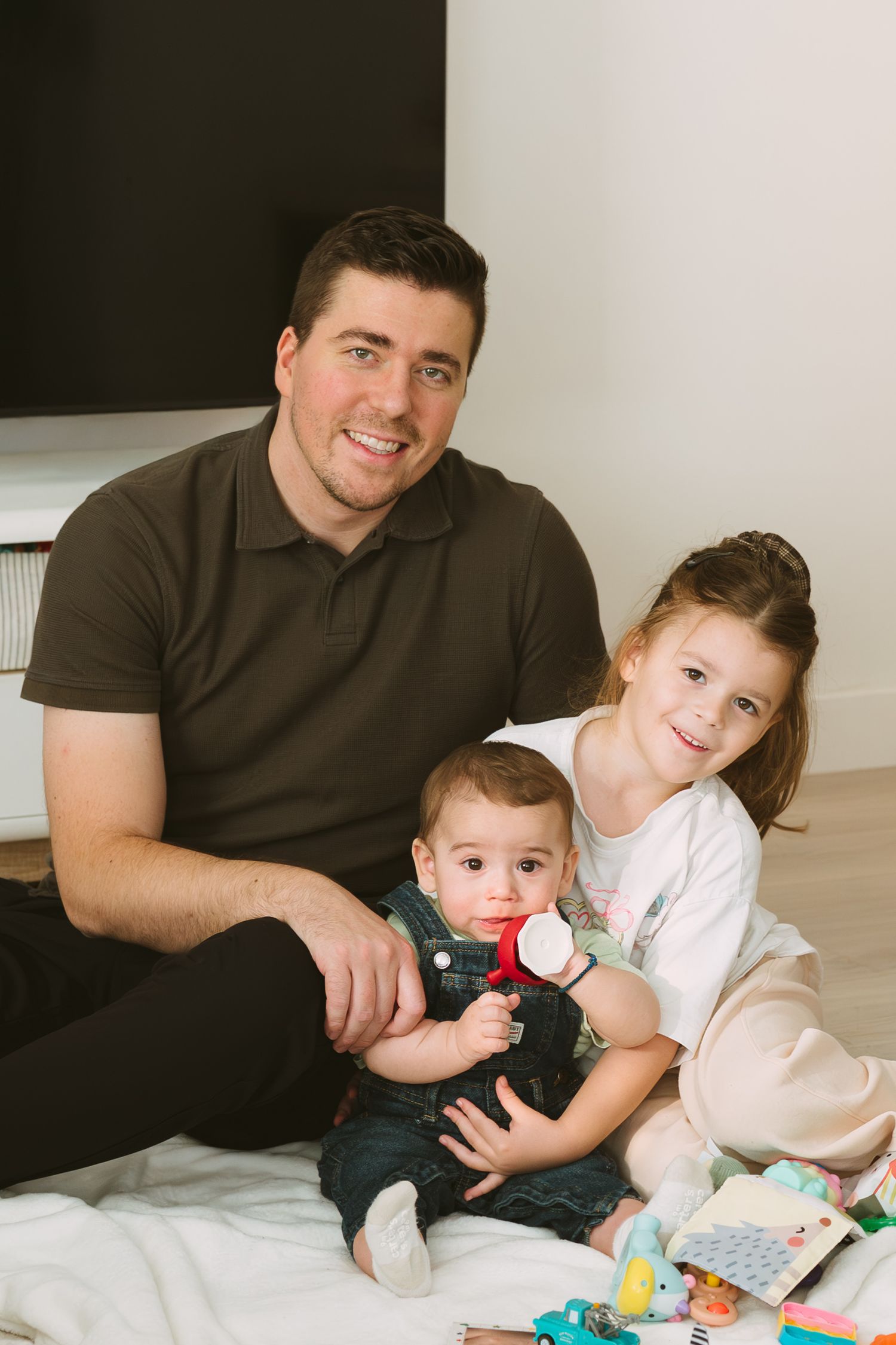 Family members sit together on a white couch while playing with colorful toys in a series of candid shots.
