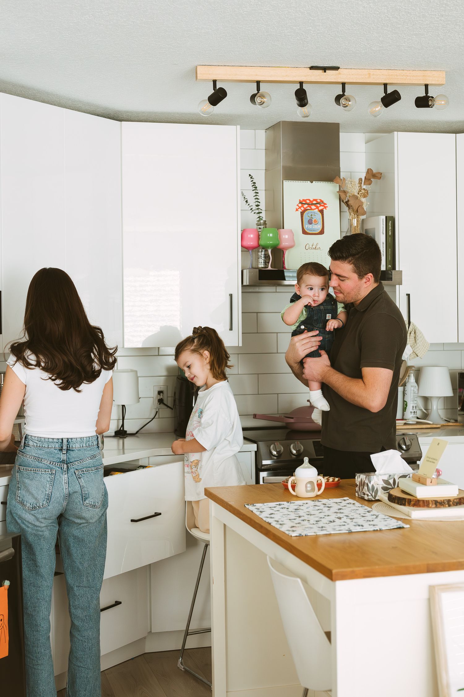 Family spending time together in a bright white kitchen while preparing food and playing.