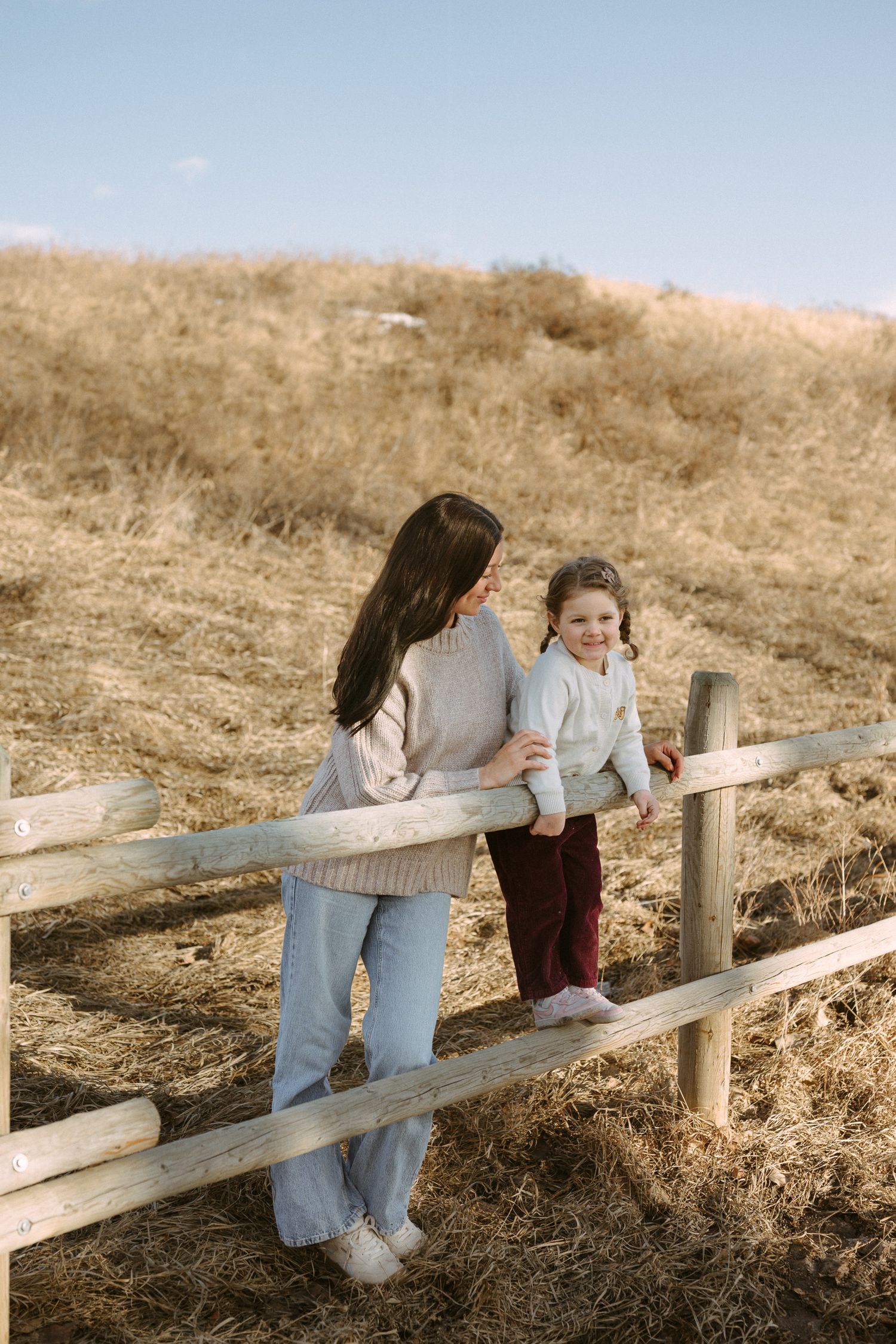 A sequence of photos showing two people playfully interacting along a wooden fence in a golden grassy field.