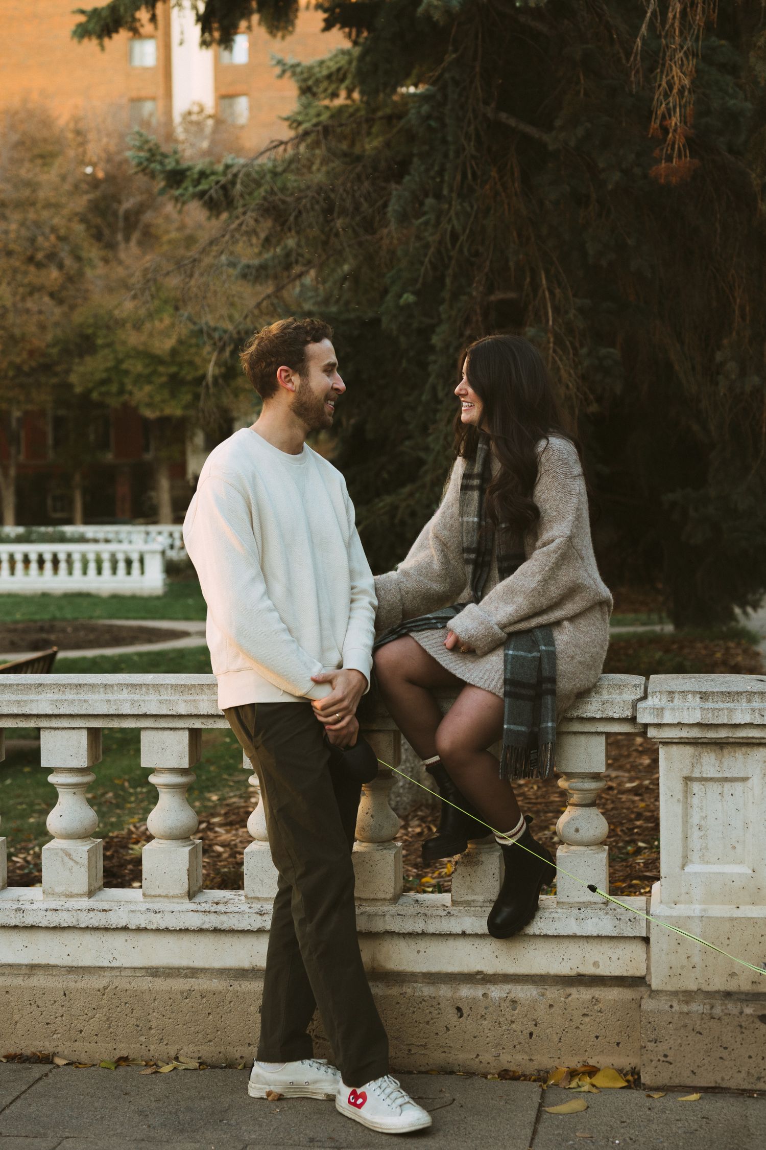 A couple sits on a stone balustrade in a park during golden hour autumn light.