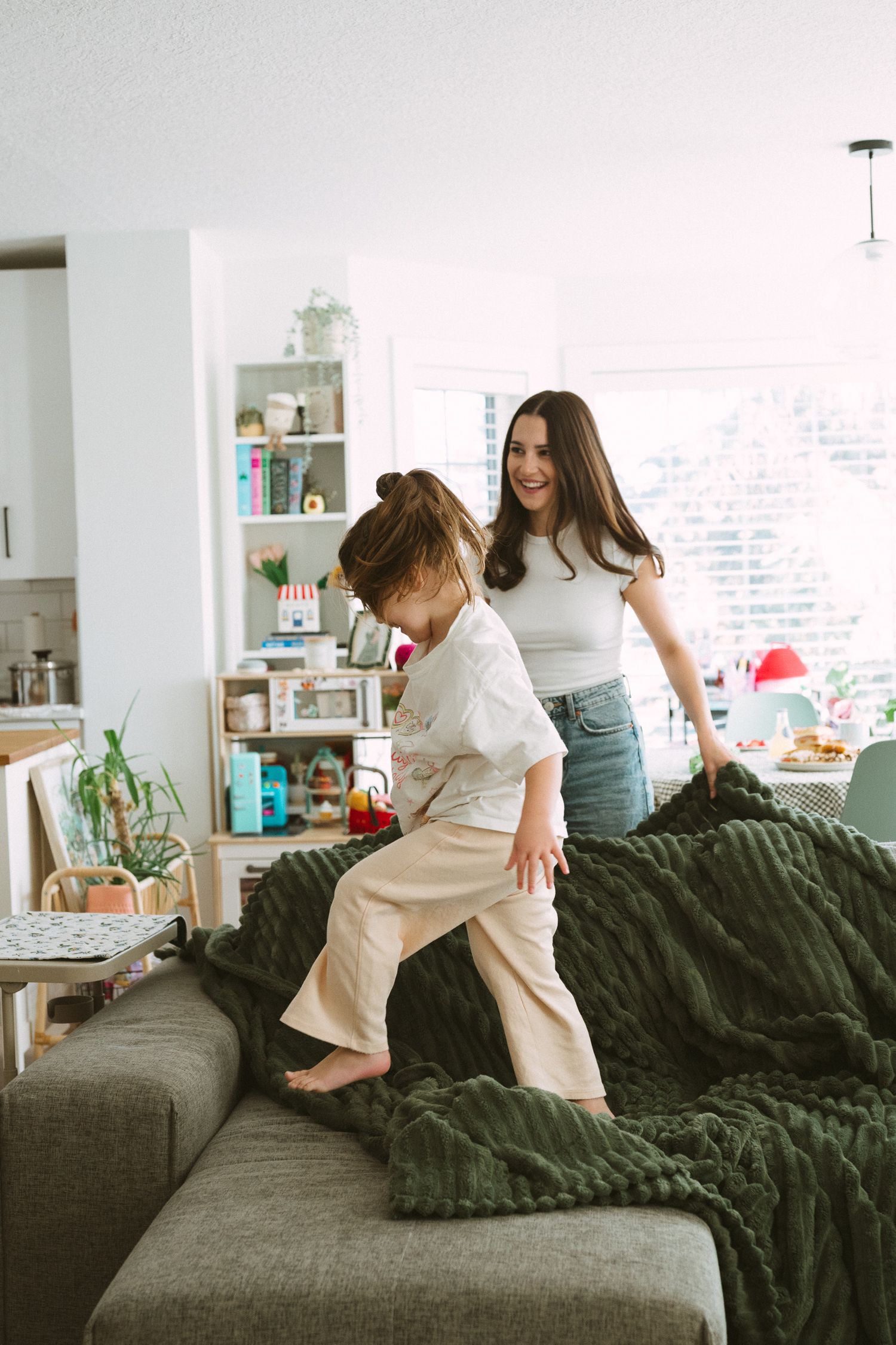A playful scene in a living room with a cozy gray couch and dark green blanket in a bright modern space.