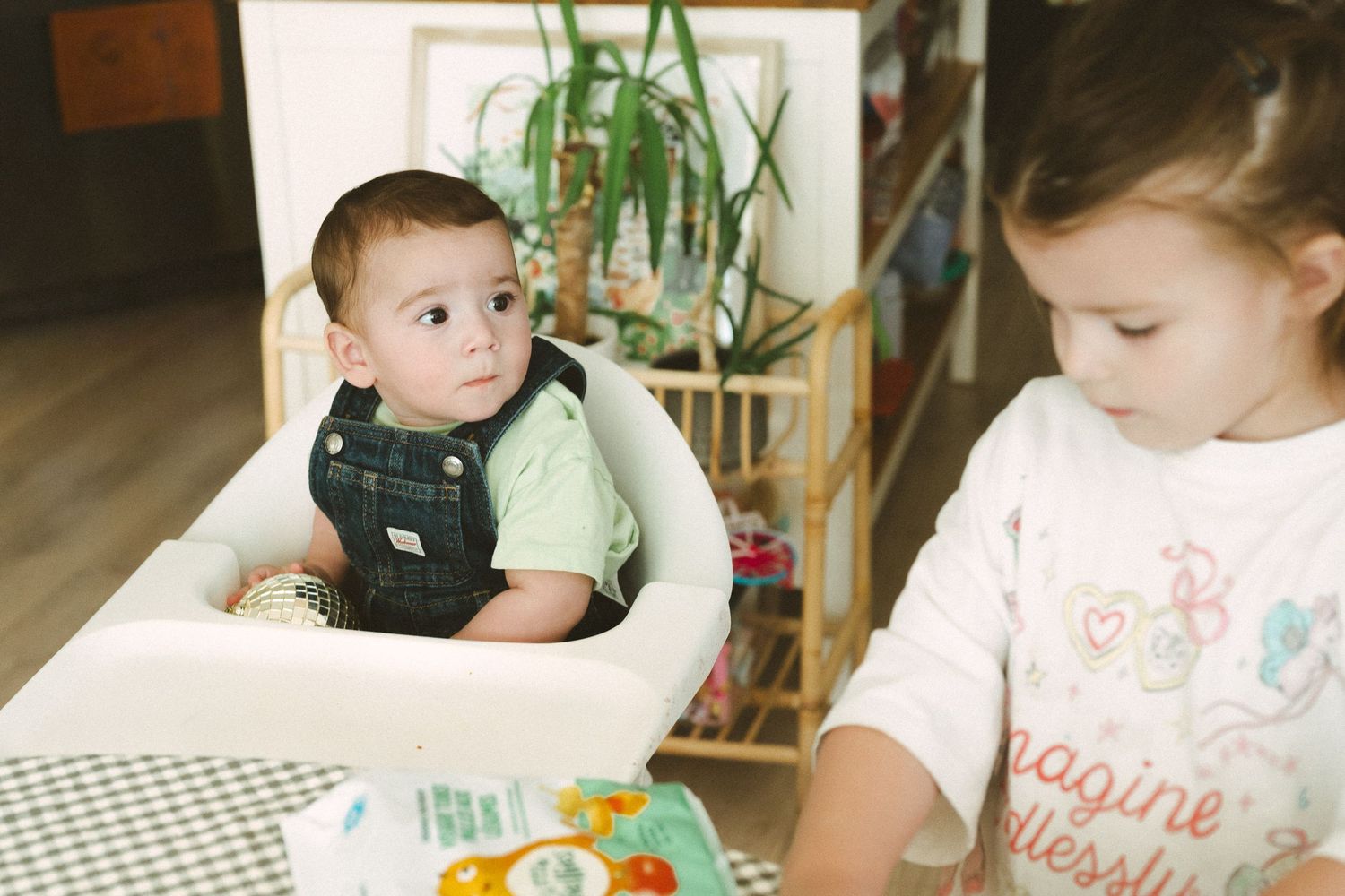 Children engaged in various activities around a dining table with plants in the background.
