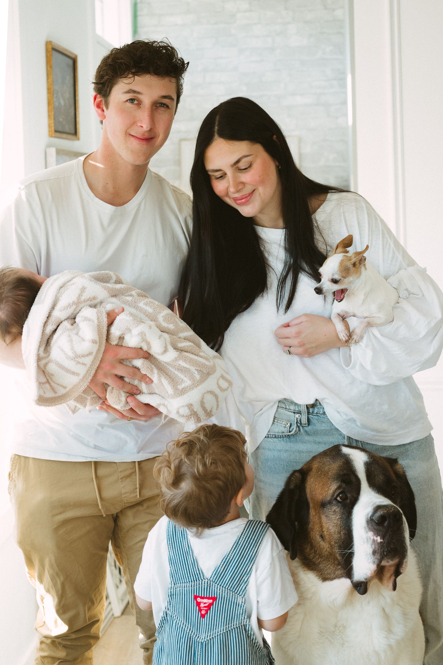 A family portrait at home with their Saint Bernard dog, baby, and toddler in overalls.