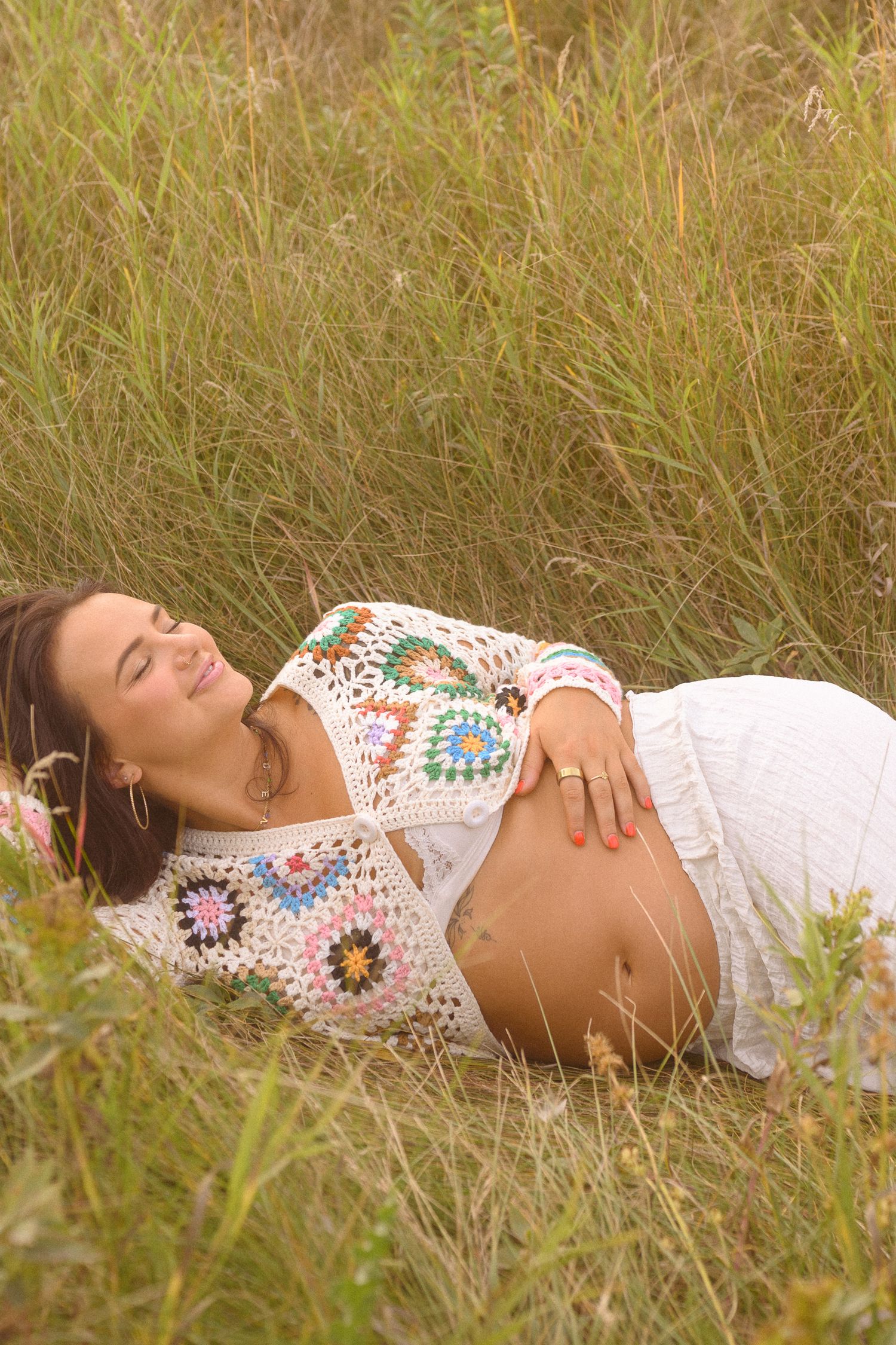 Serene maternity portrait in tall grass showcasing vintage-inspired crochet and white dress.