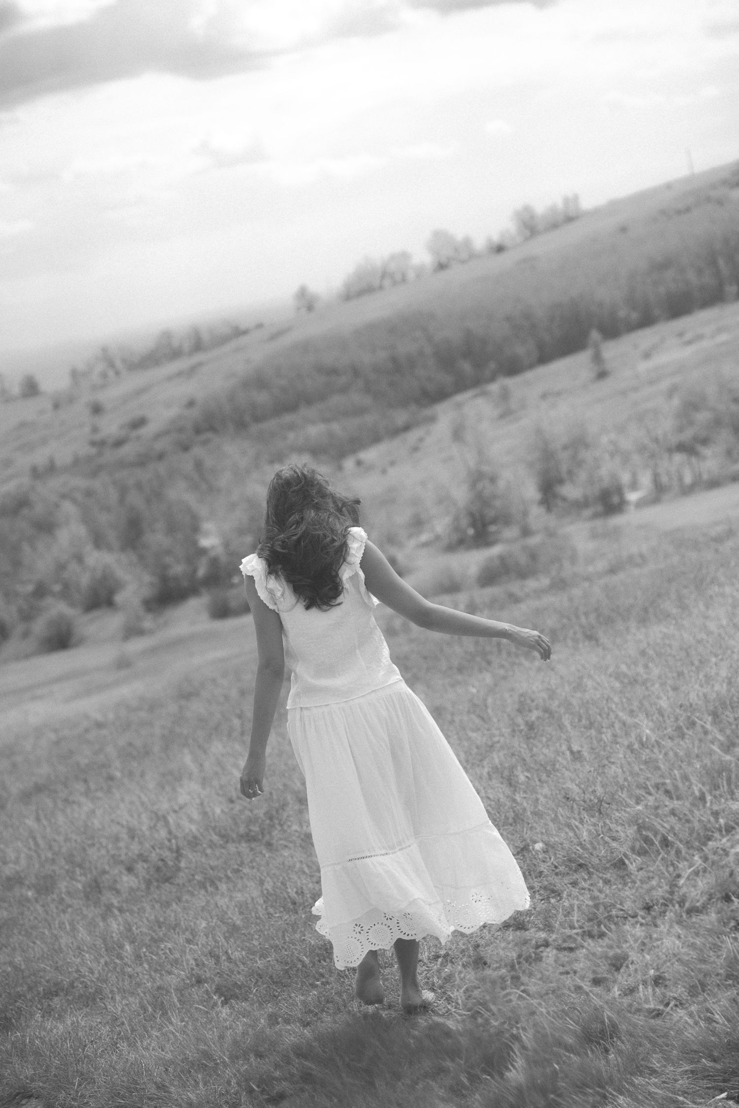 A flowing white dress twirls on a grassy hillside in black and white photography.