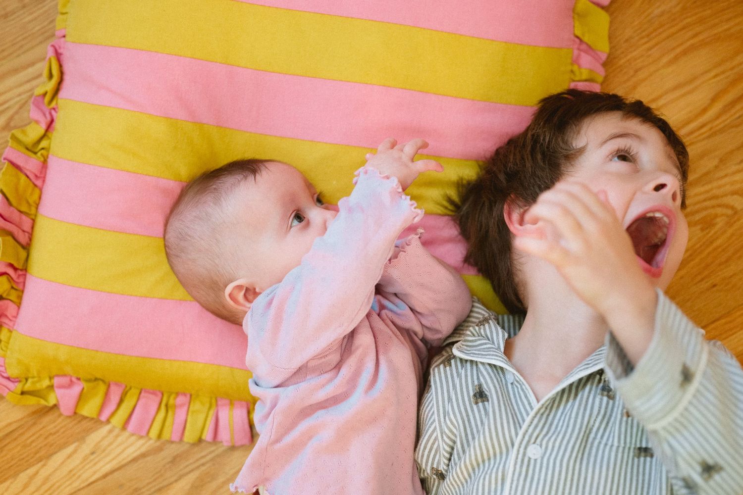 Two children laying on pink and yellow striped cushion showing playful expressions.
