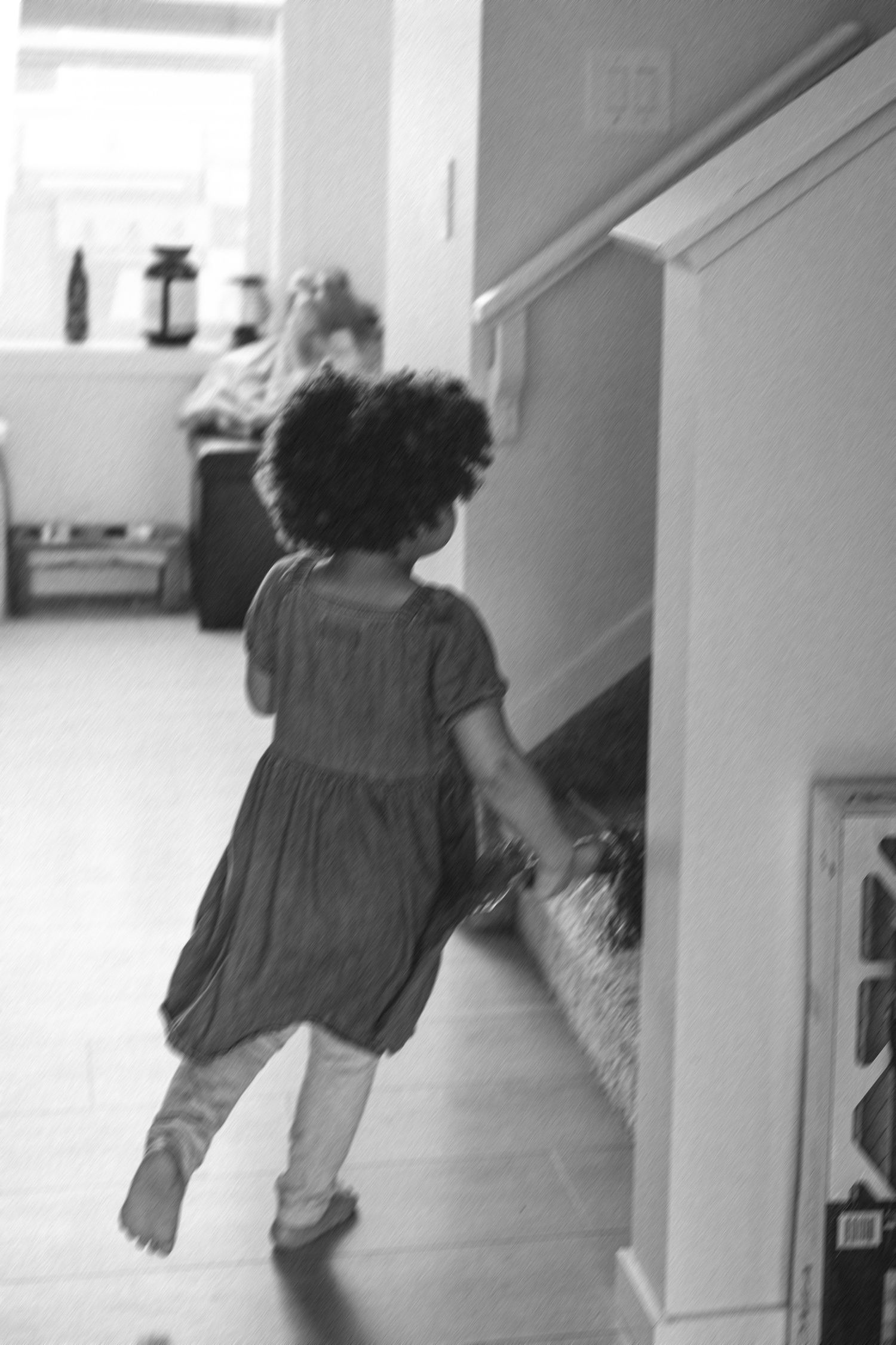 Young toddler girl with curly hair in dress running through home hallway.