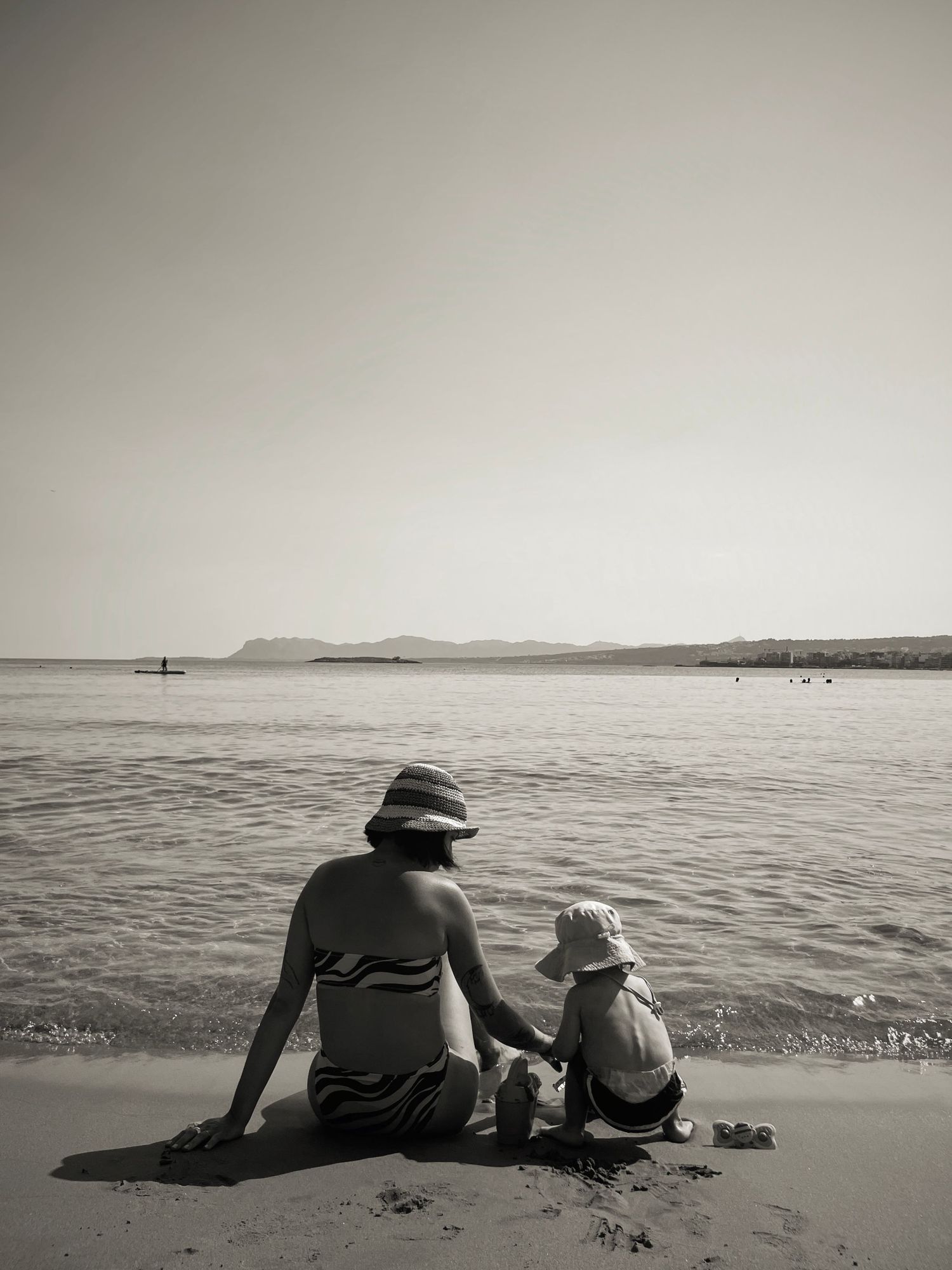 Black and white beach scene with two figures sitting on sand watching the ocean.