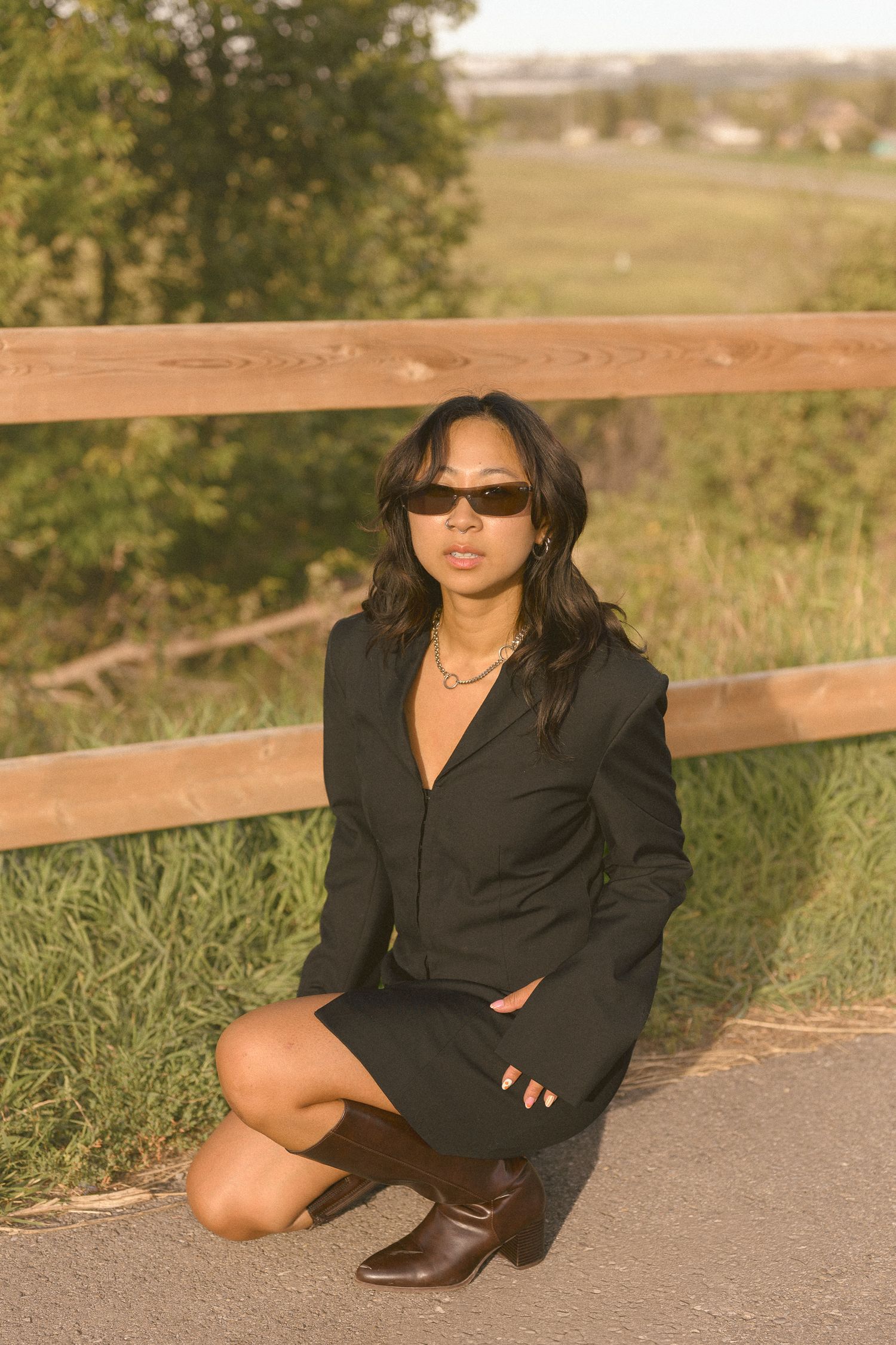 A chic black blazer dress styled with sunglasses and boots in an outdoor setting.