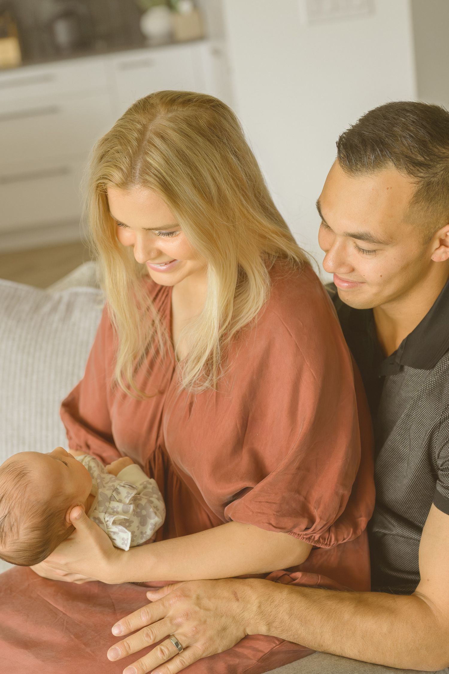 Parents sharing intimate moment with newborn baby on couch.