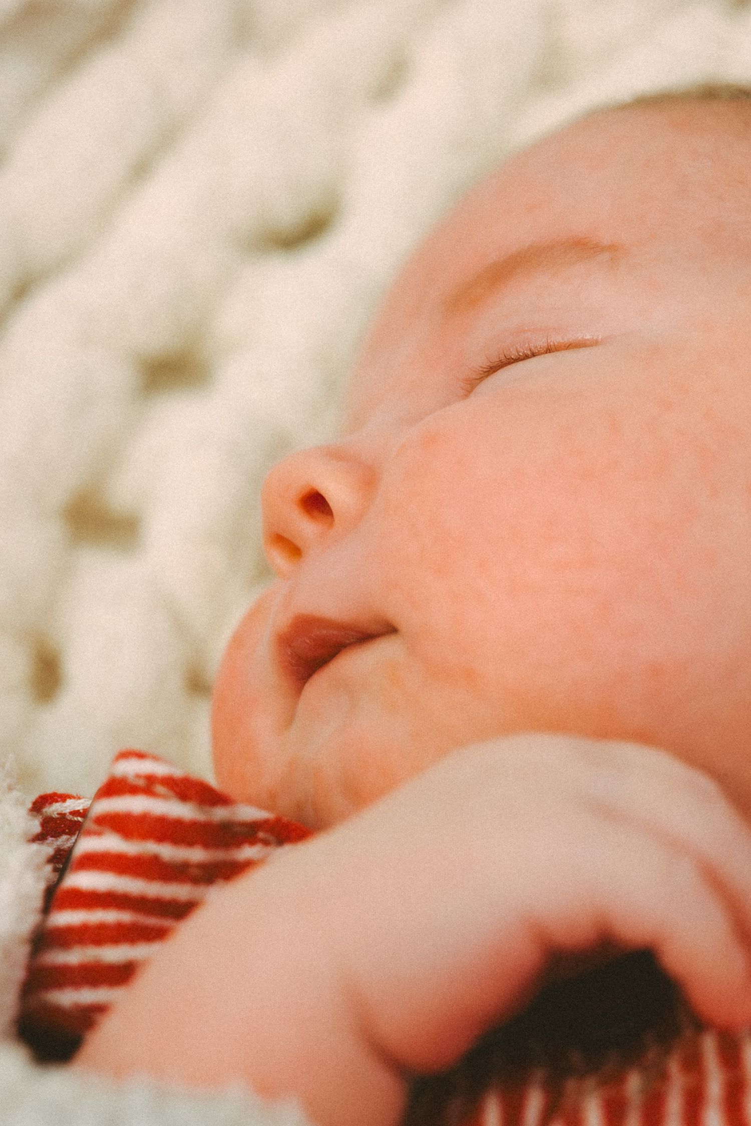 A sleeping infant wearing red and white striped clothing rests peacefully on a white blanket.