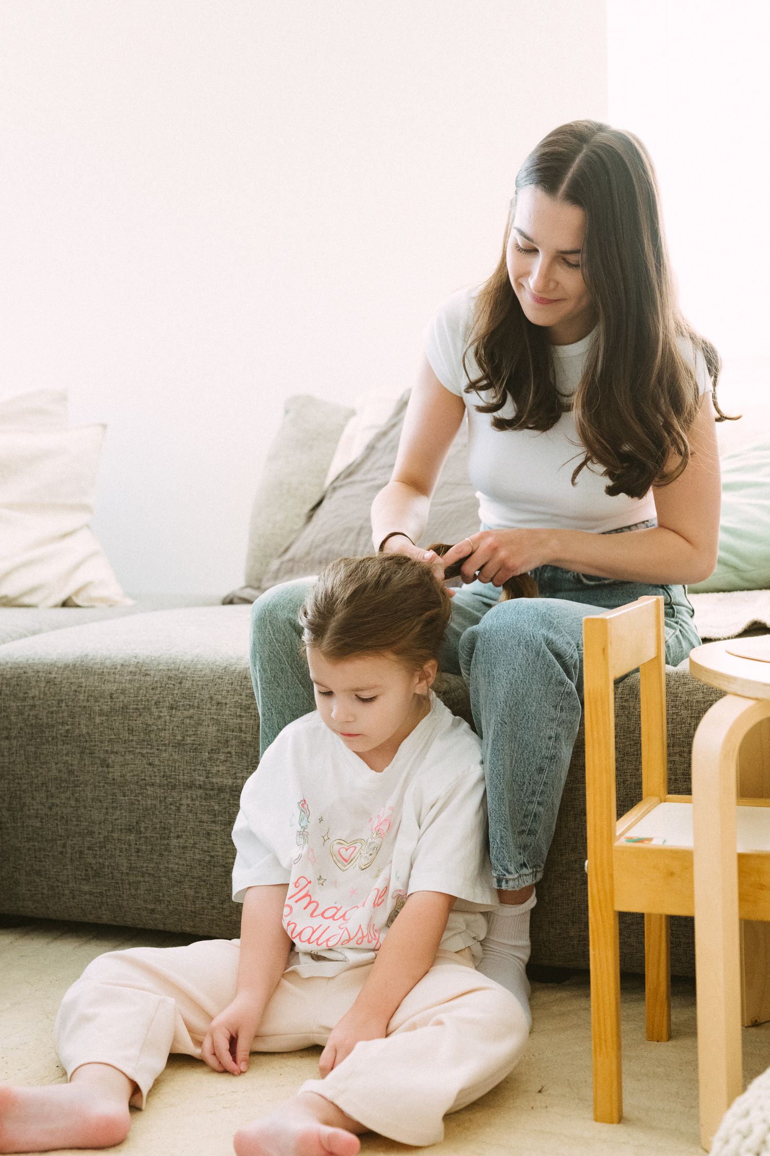 Mother and daughter sitting together on grey couch while reading and bonding at home.