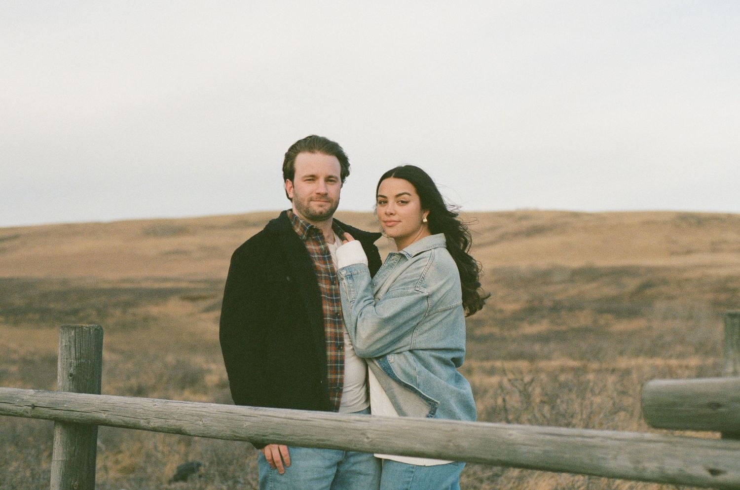 A couple embraces while standing in front of a scenic desert landscape during golden hour.