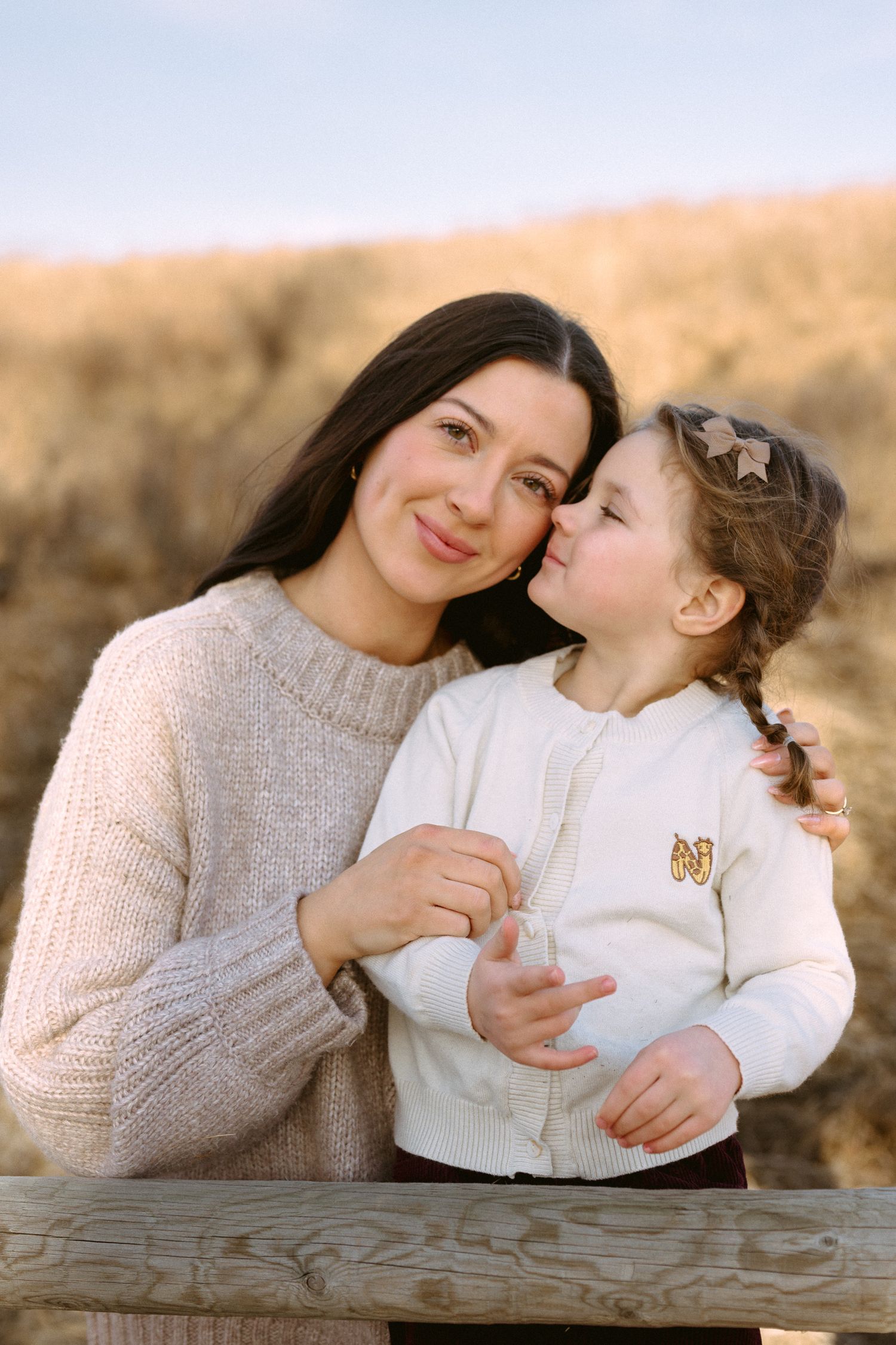 Intimate portrait of parent and child embracing by wooden railing in warm sunset light.