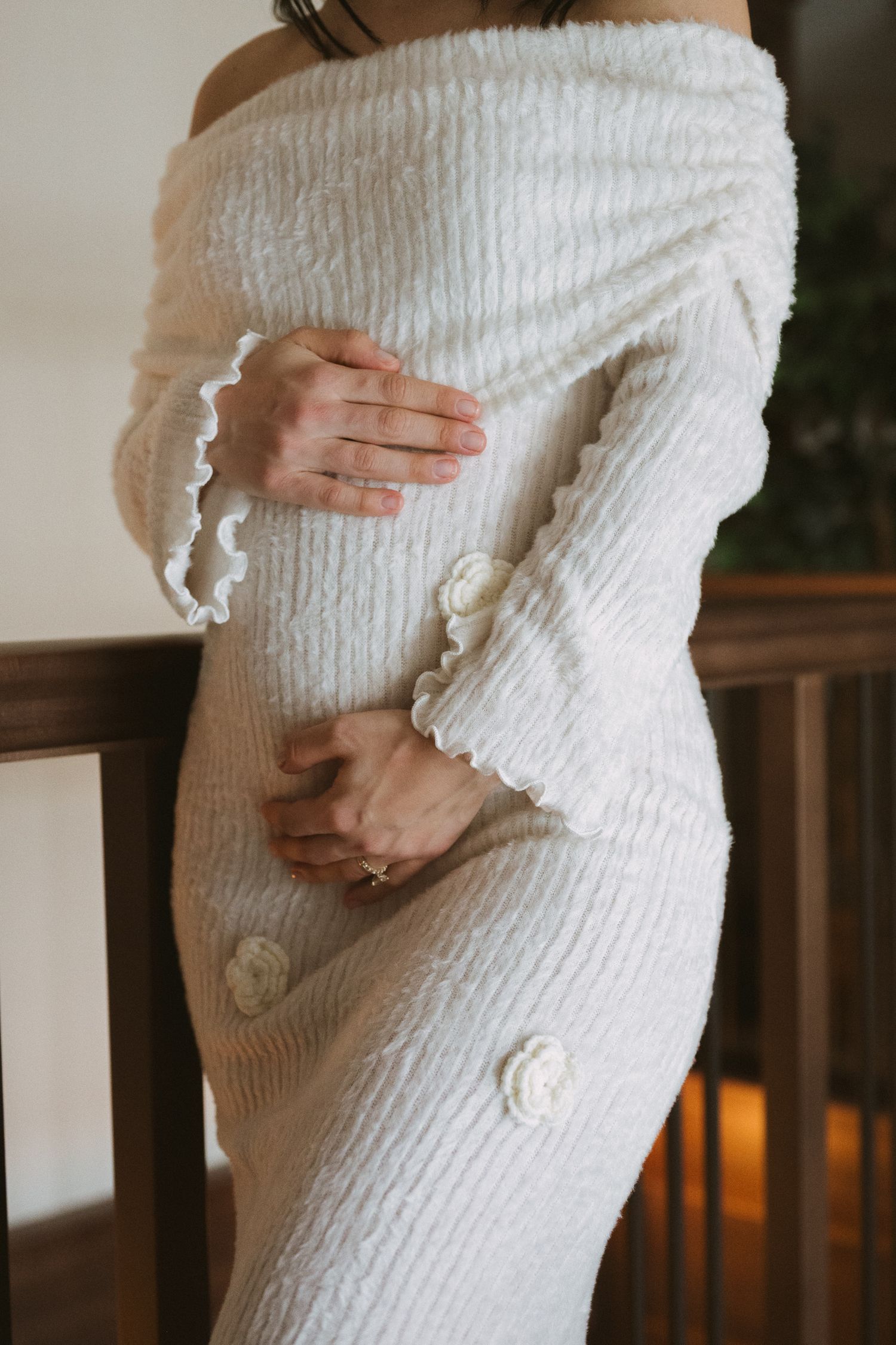 Close-up of pregnant woman in white off-shoulder textured knit maternity dress with floral button details.