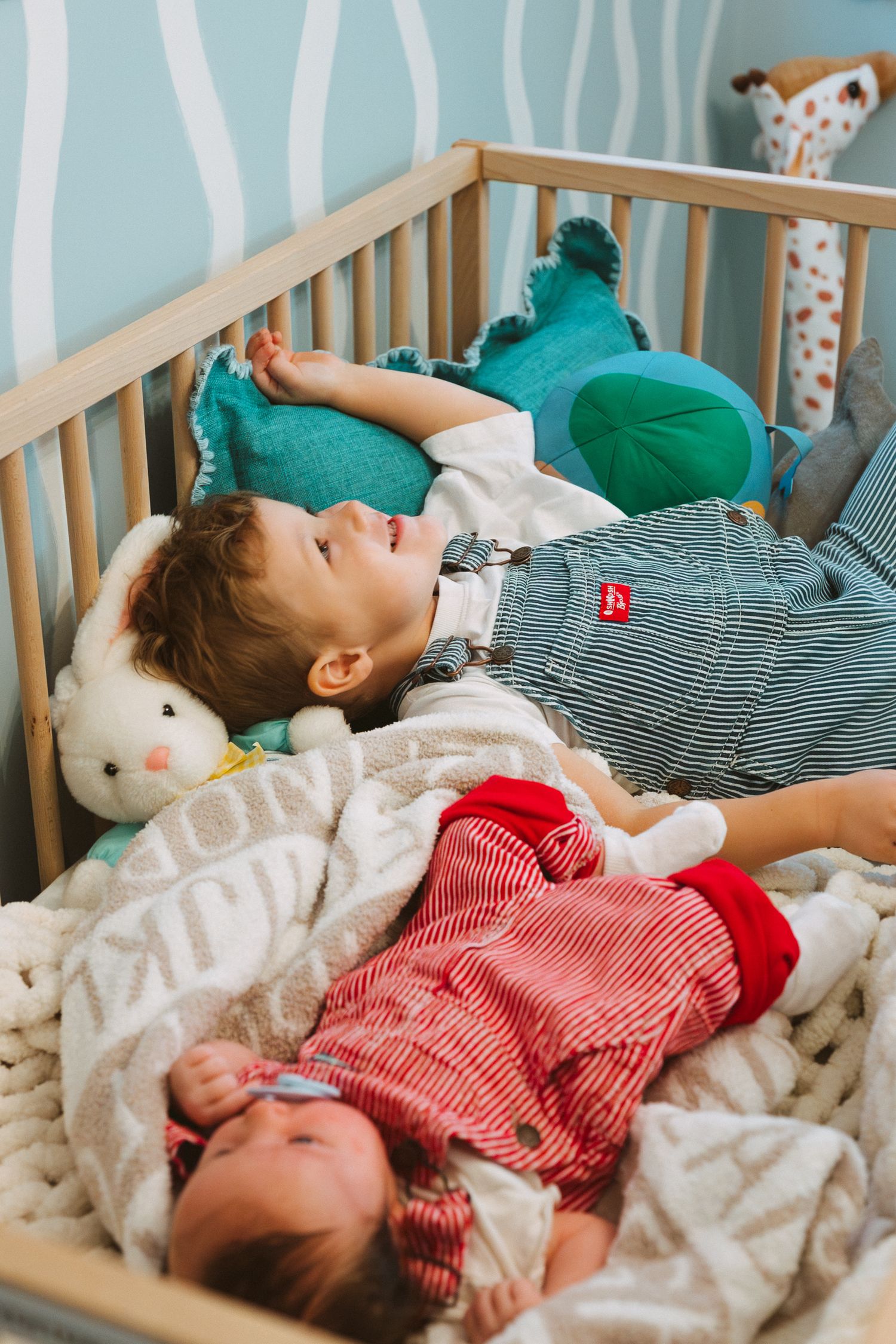 Child resting peacefully in a turquoise-themed nursery crib with stuffed animals.