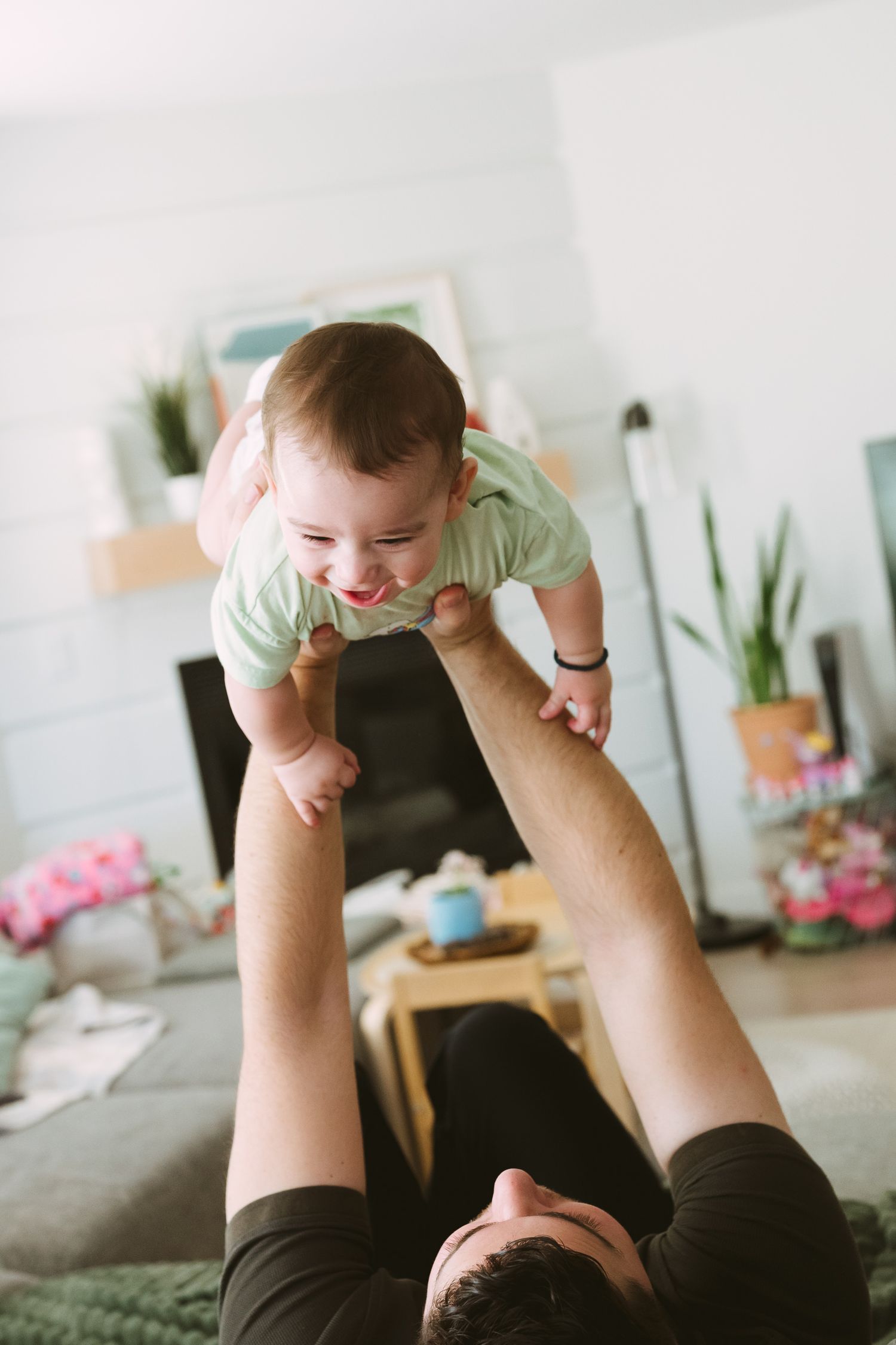 Playful moments captured in a bright living room with indoor plants and pink flowers visible.