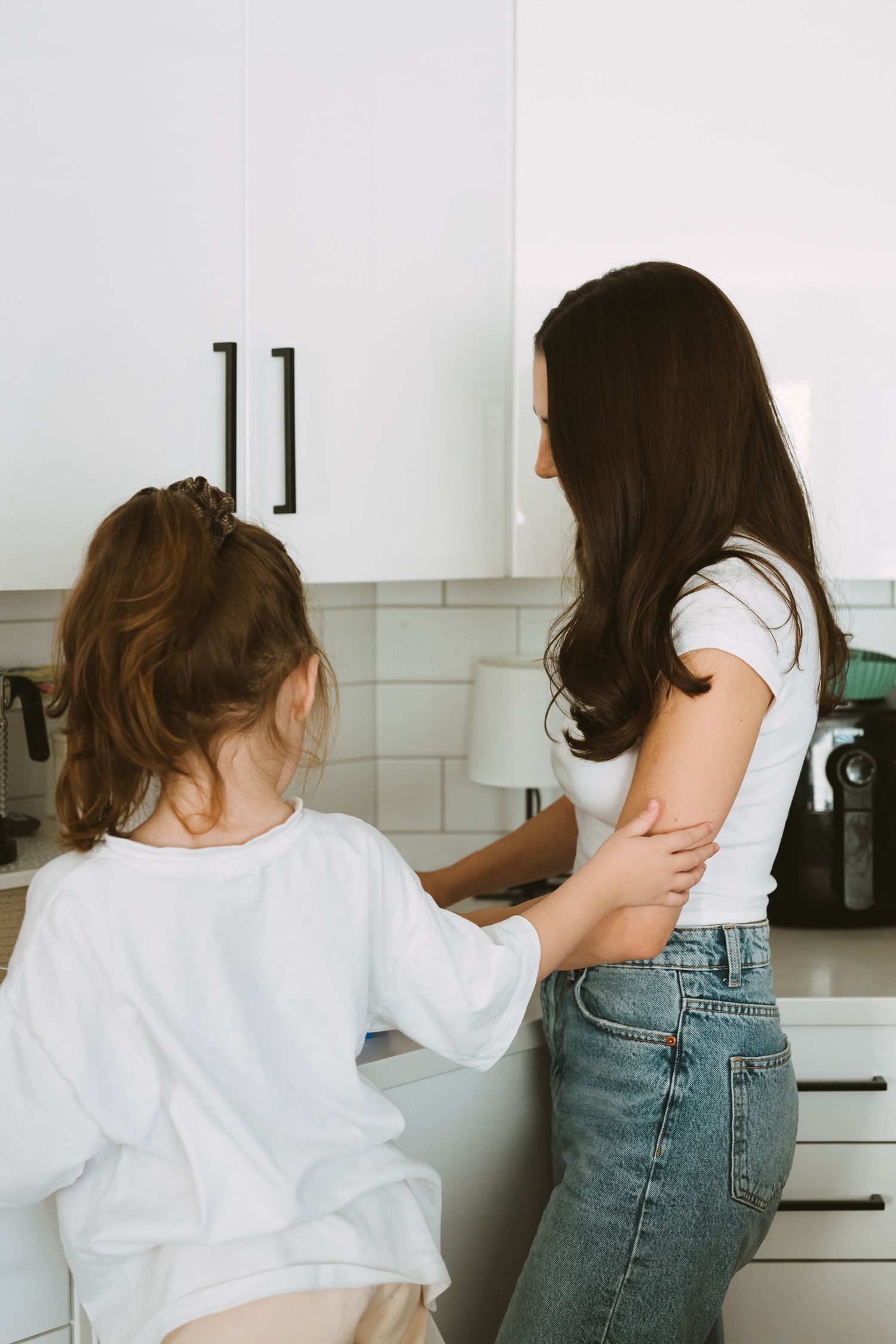 Series of photos showing someone in white shirt and jeans looking inside kitchen cabinets.