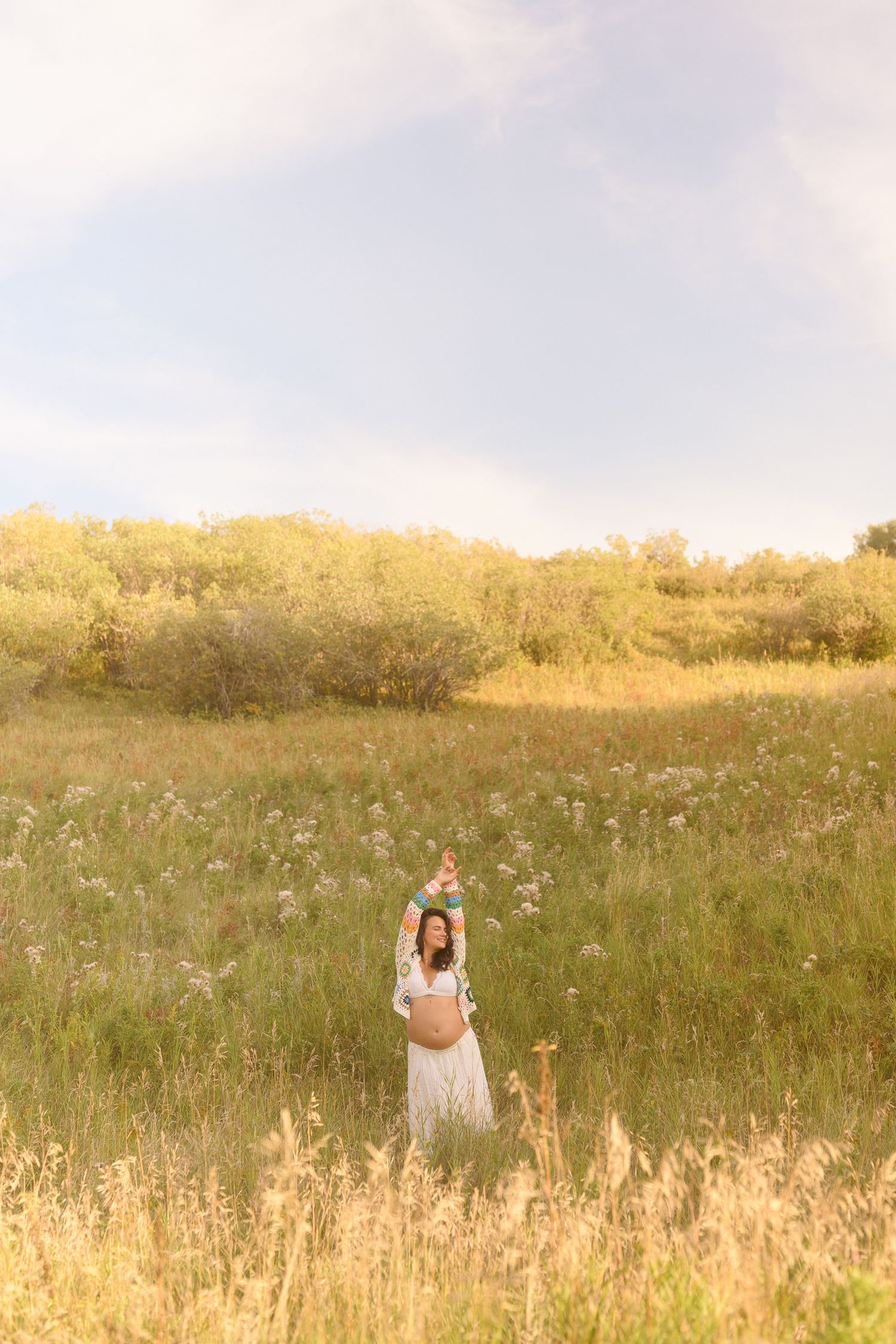 A serene maternity portrait taken in a sun-drenched field with wildflowers and natural lighting.