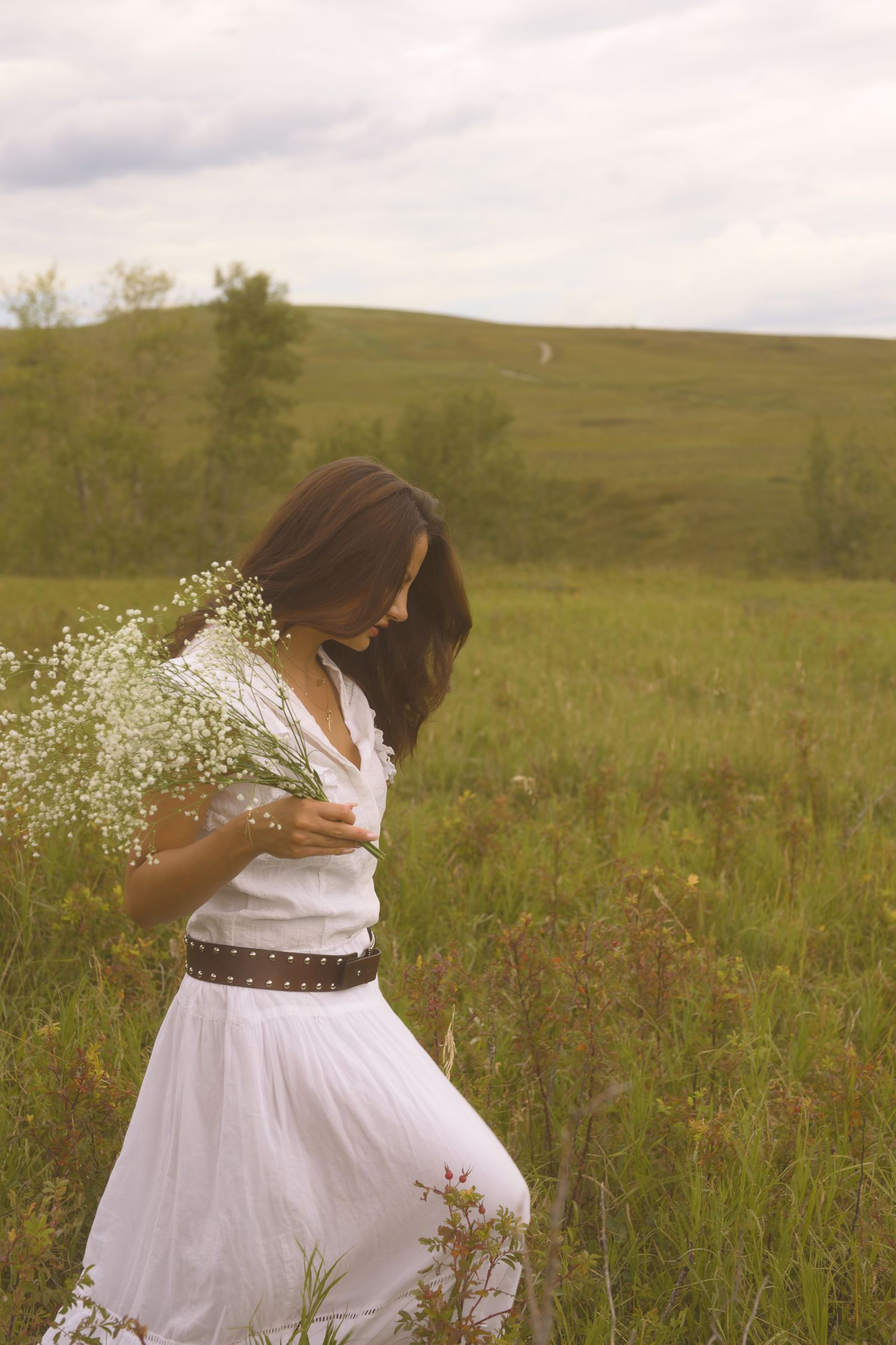 A figure in flowing white spins with baby's breath flowers in a sunlit meadow.