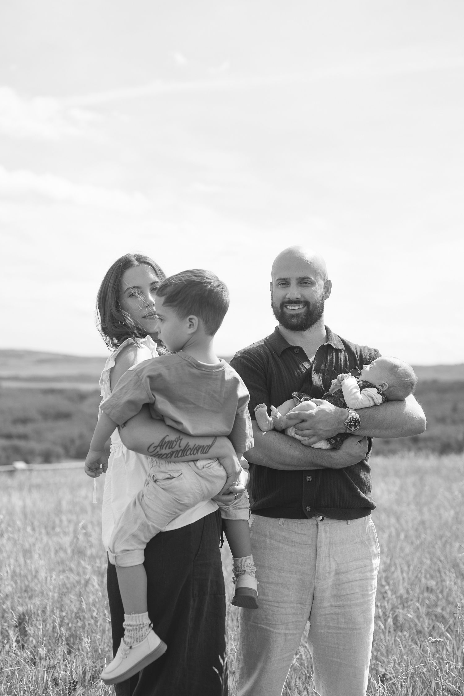 A family embraces in a field during a sunset photoshoot, creating a warm and intimate outdoor portrait.