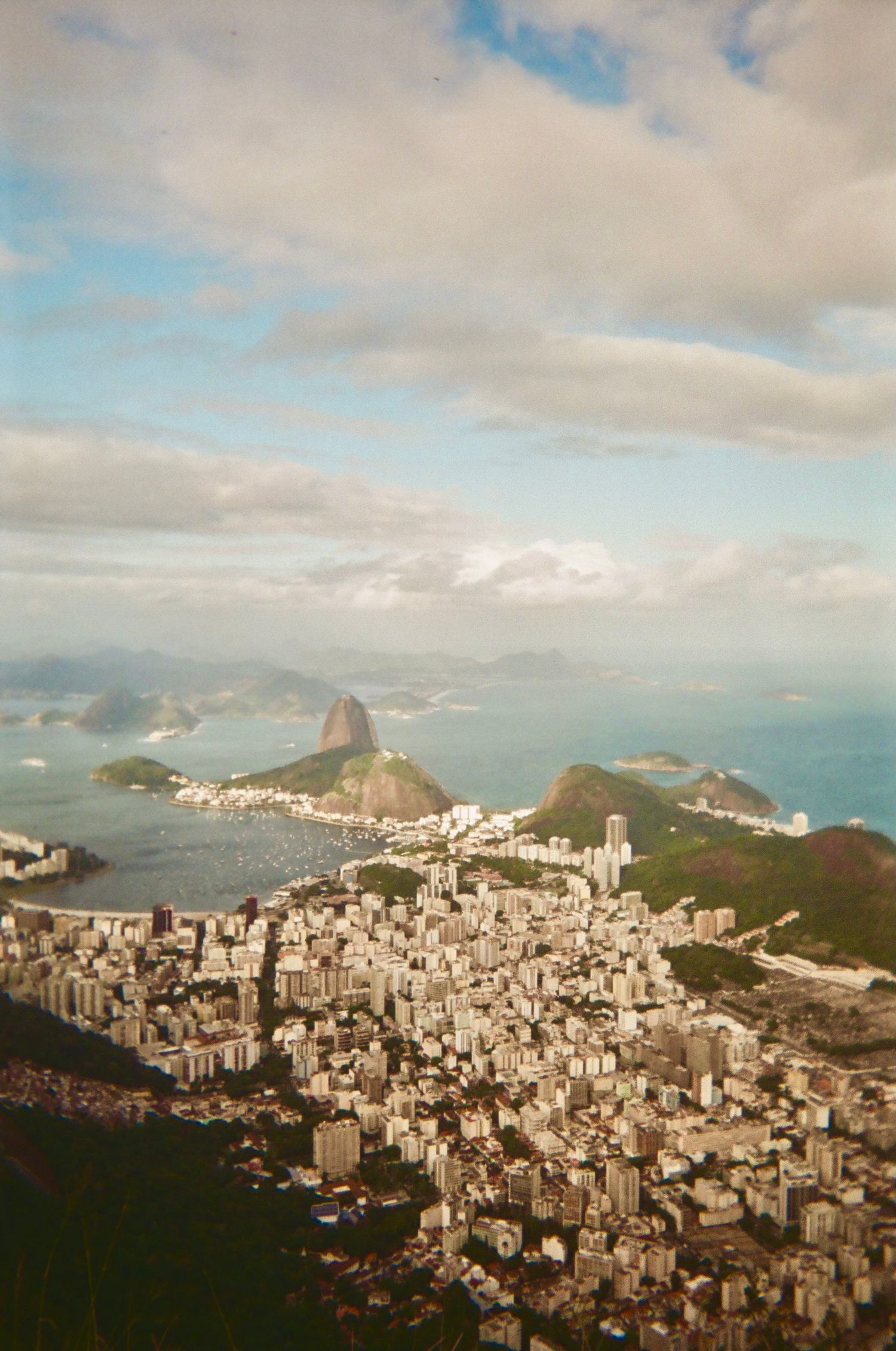 Panoramic cityscape view of Rio de Janeiro with mountains and coastline under cloudy skies.