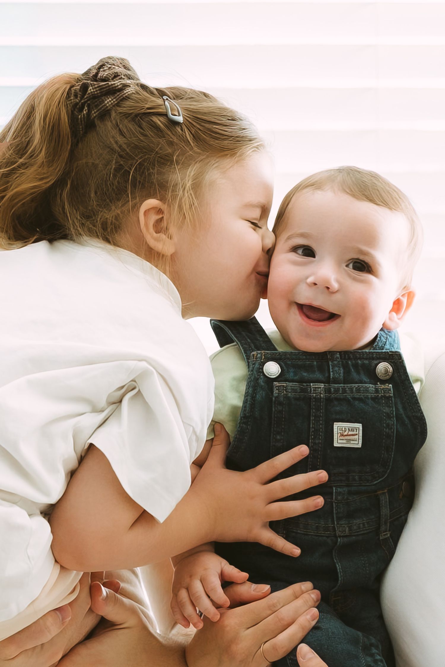 Two young children sharing a sweet moment together while sitting on white furniture.