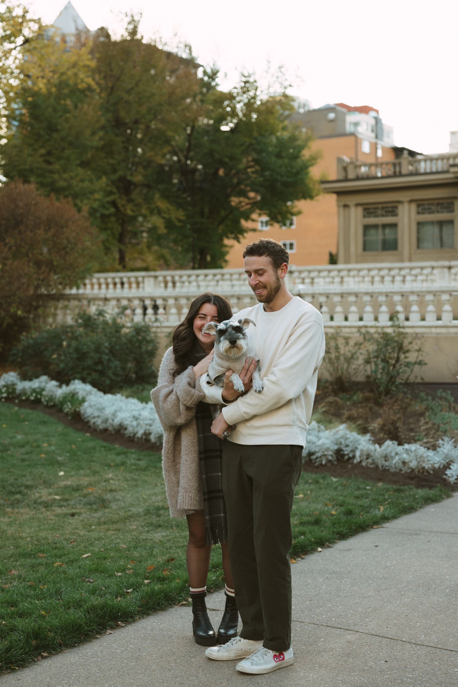 Couple laughing together on a garden path with ornate white railings and autumn foliage.