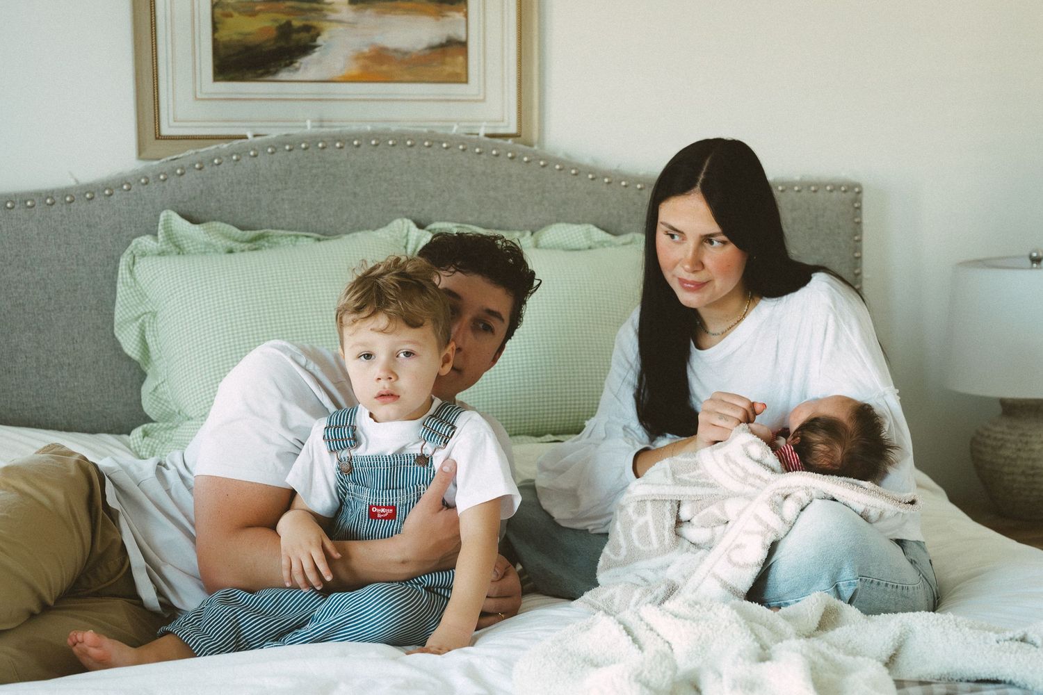 A family relaxes together on a cozy gray couch with mint green pillows in a bright, sunlit room.
